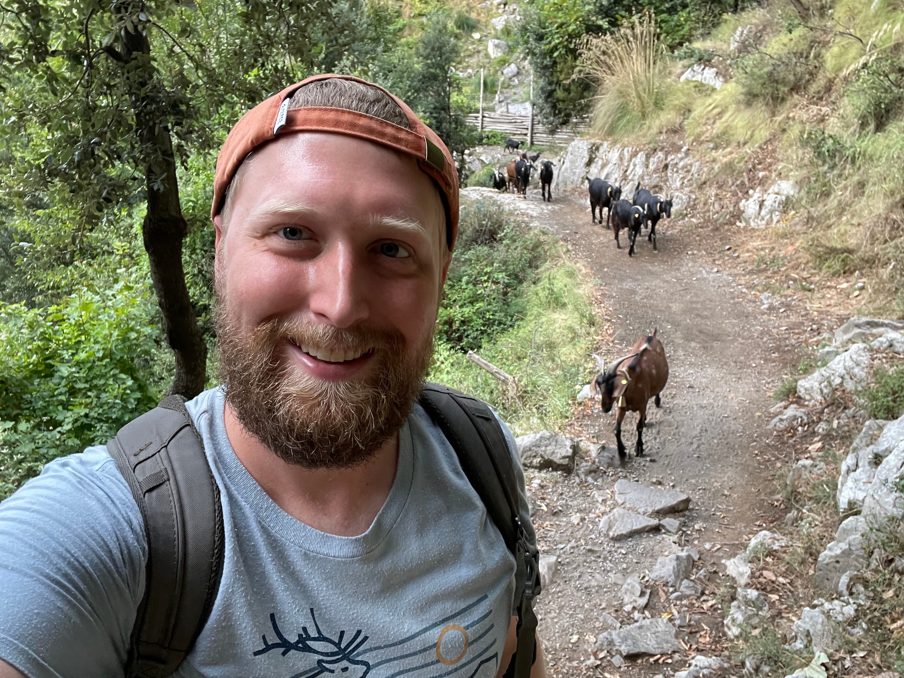 Timothy posiert für ein Selfie, während ihm Ziegen folgen.