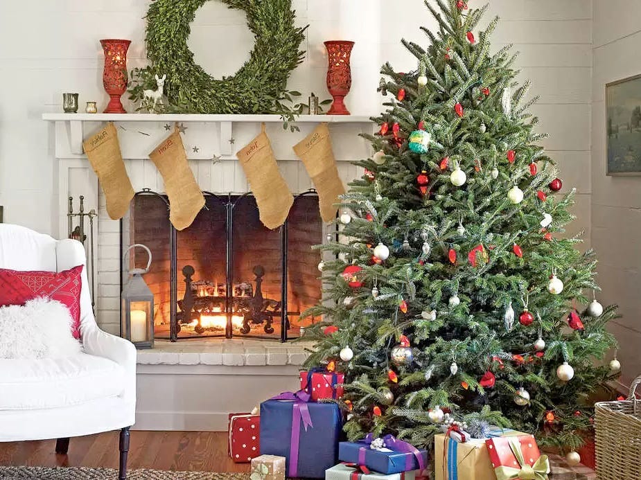 Ein „Tree to Your Door“-Weihnachtsbaum mit vielen Geschenken darunter neben einem Kamin.