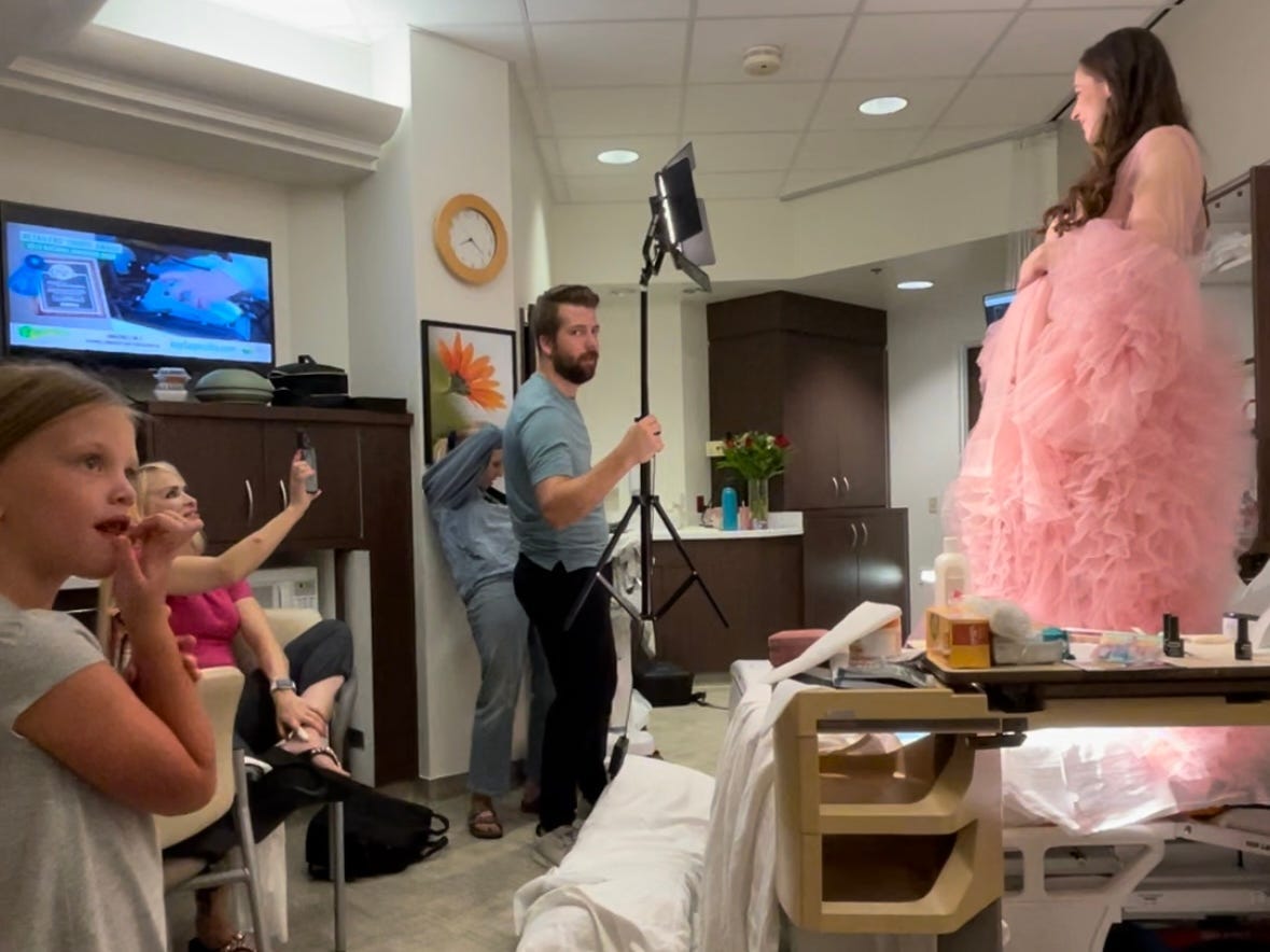 Jackie Kunzelman posiert in einem fließenden rosa Kleid für ein Schwangerschaftsfotoshooting auf ihrem Krankenhausbett.