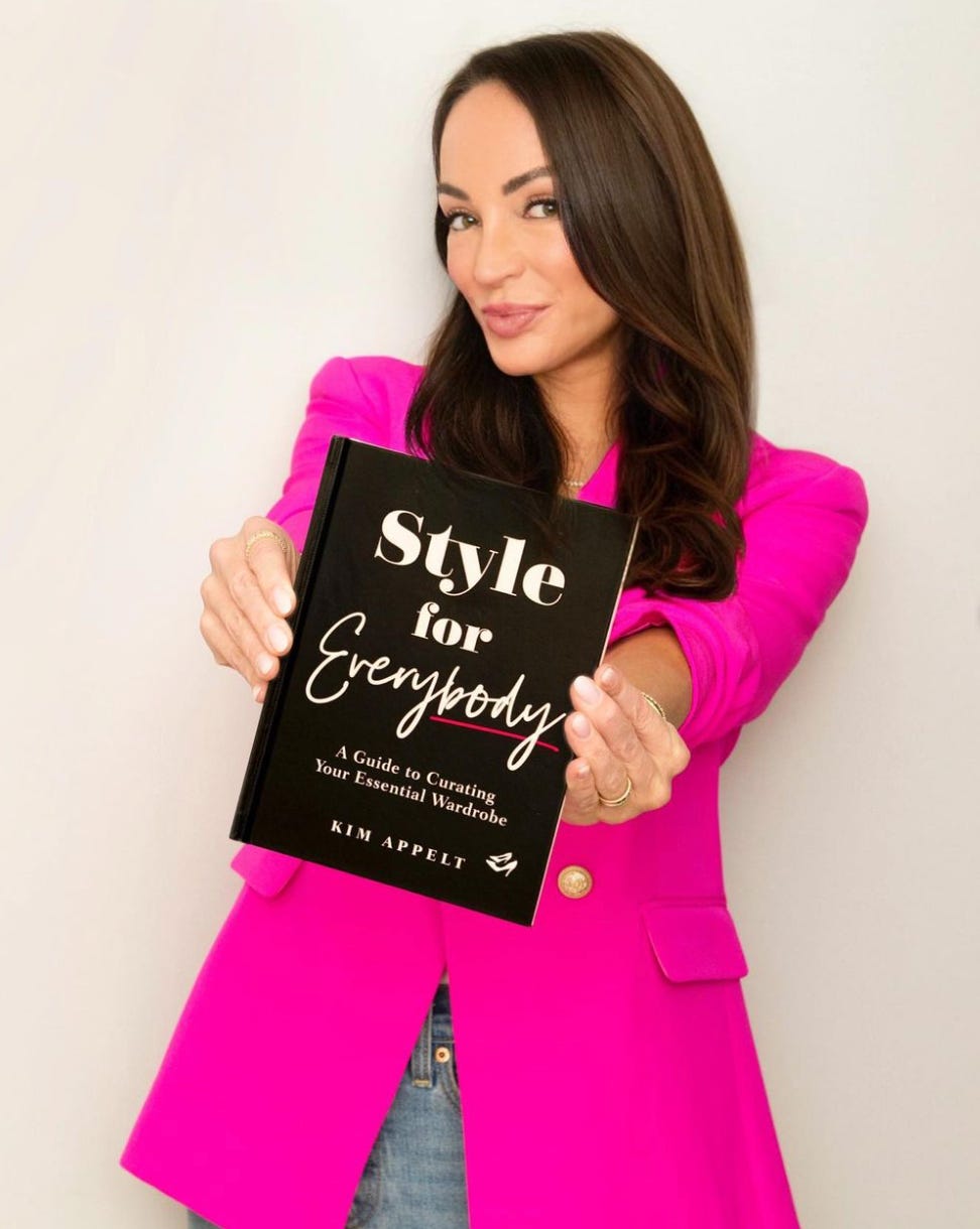 Die Stylistin im rosa Blazer hält ihr Buch „Style for Everybody“ vor weißem Hintergrund hoch
