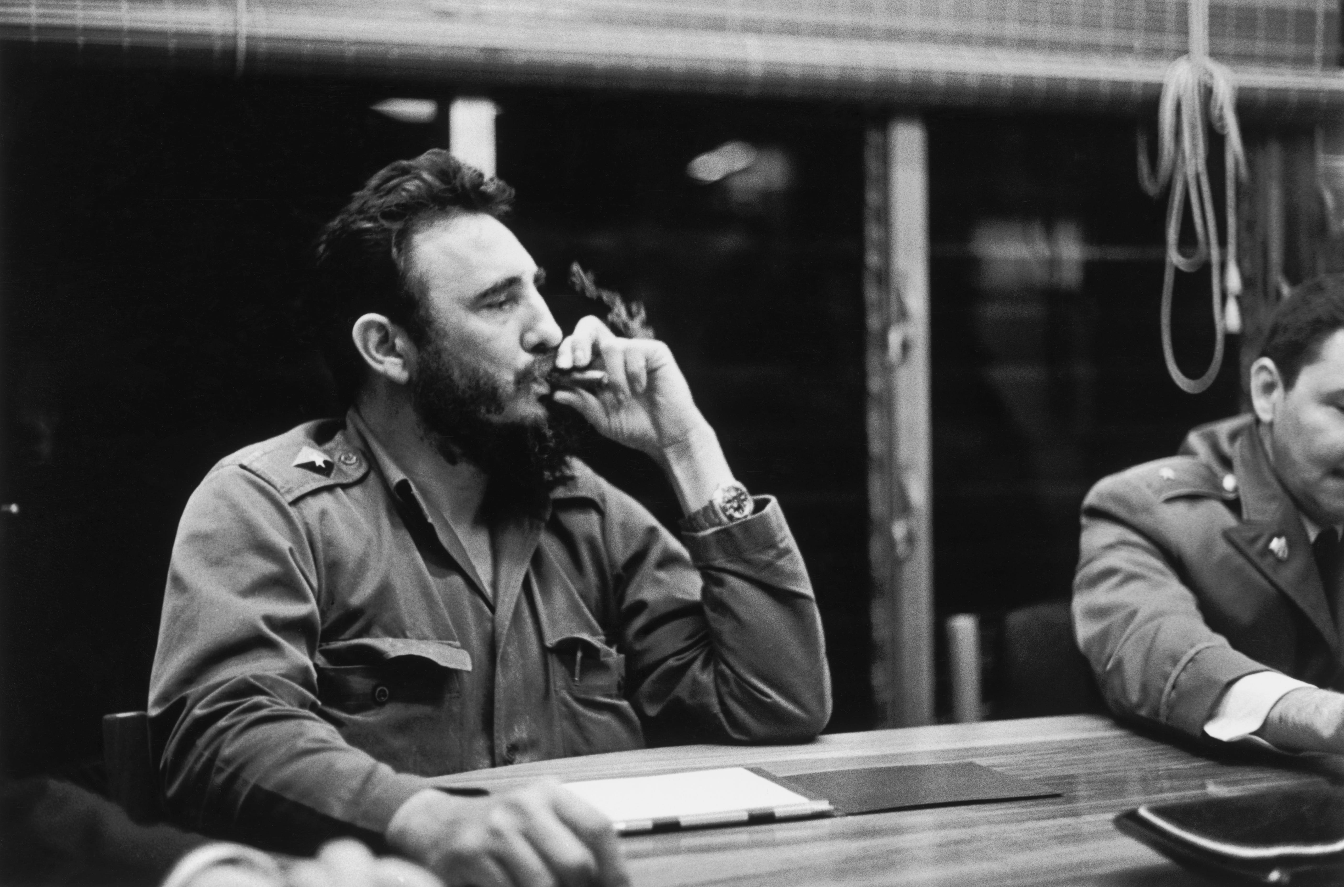 Ein Foto von Fidel Castro, der in einer Besprechung sitzt und einen Zug von seiner Zigarre nimmt.