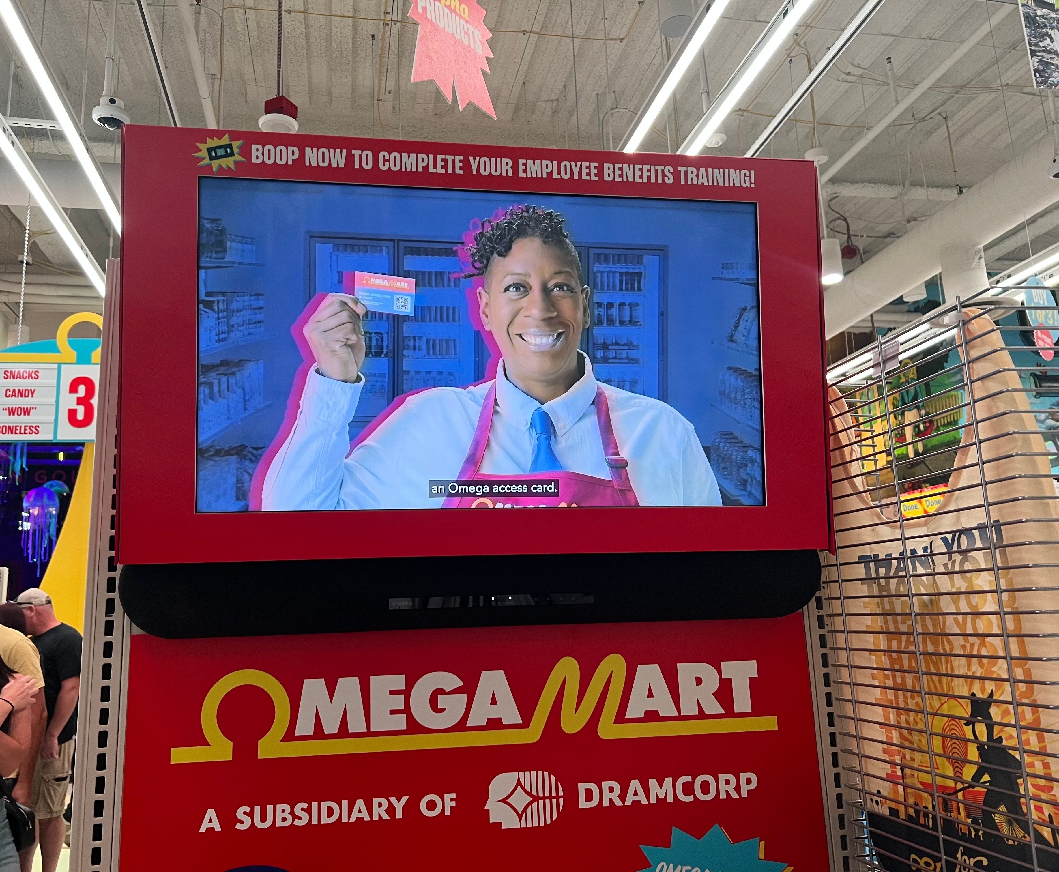Ein Fernsehbildschirm mit einem Omega-Mart-Mitarbeiter, der eine Karte in der Hand hält.
