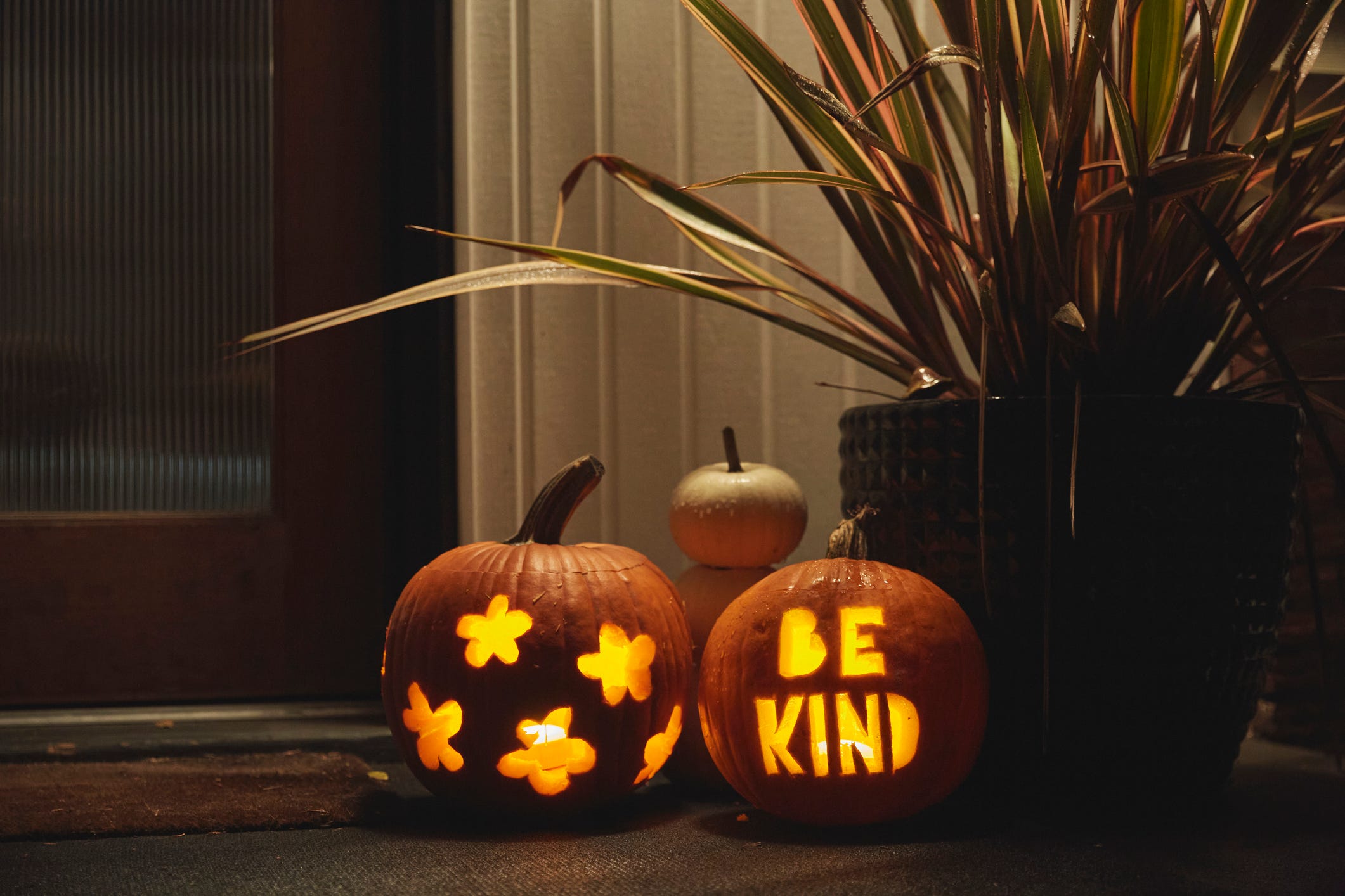 Zwei beleuchtete Kürbisse auf einer Veranda, einer mit der eingravierten Aufschrift „Sei freundlich“.