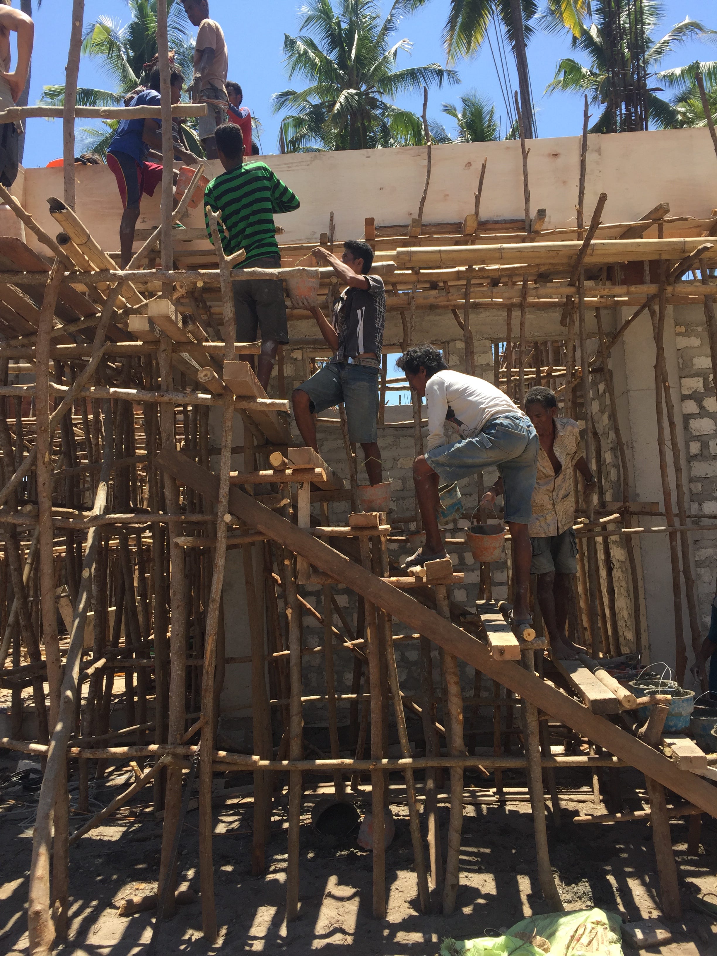 Eine Gruppe von Männern auf einer Baustelle reicht sich gegenseitig Eimer mit Zement eine Holztreppe hinauf