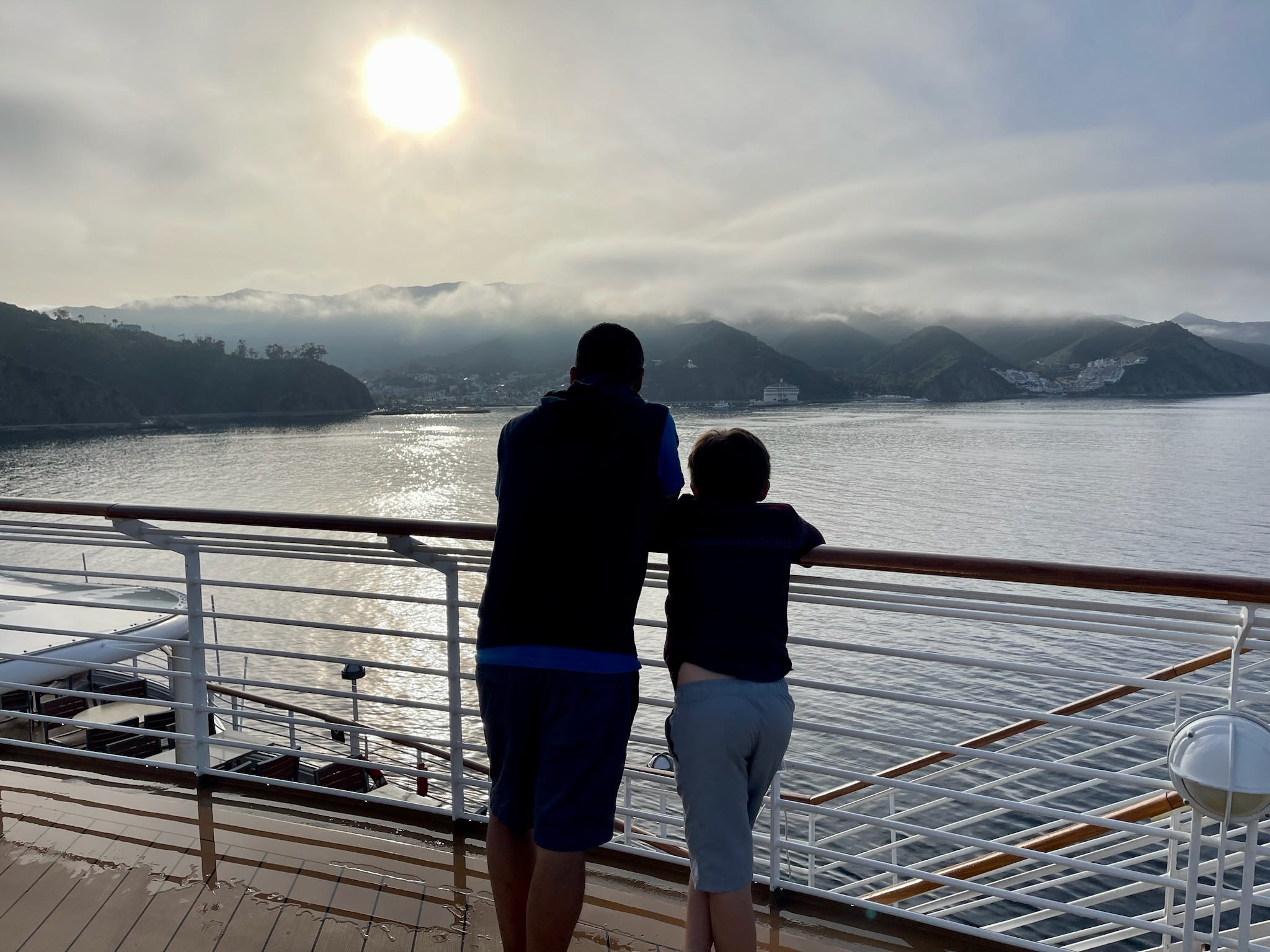 Der kleine Sohn des Autors und sein Vater blicken über die Reling eines Kreuzfahrtschiffbalkons in die Sonne