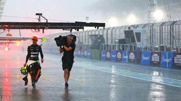Lando Norris von McLaren geht zurück zur McLaren-Box, gefolgt von einem Kameramann, während in Interlagos heftiger Regen fällt