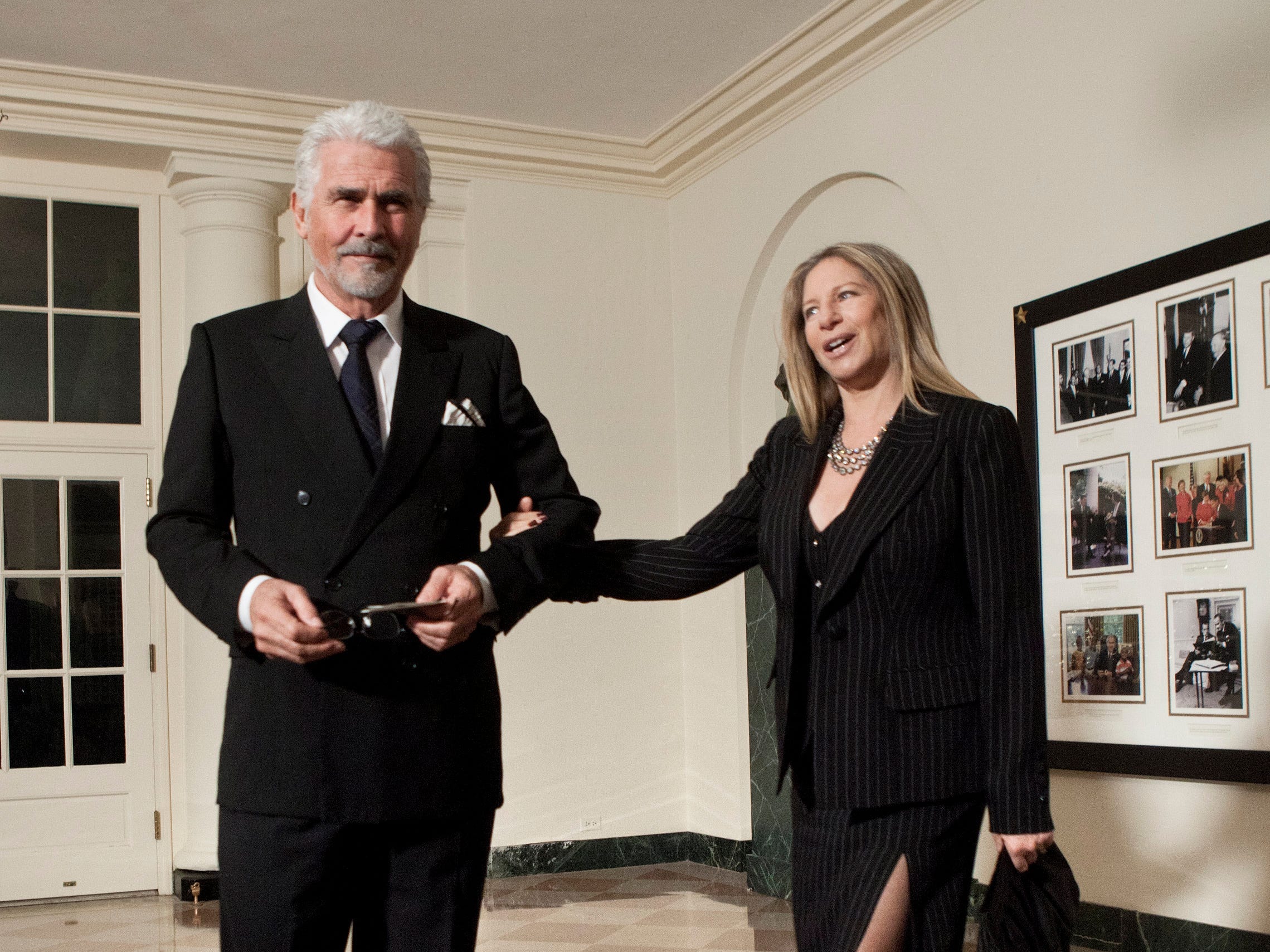 James Brolin steht in einem schwarzen Anzug vor einem Staatsessen im Weißen Haus, zusammen mit seiner Frau Barbra Streisand in Nadelstreifenjacke und Kleid, die ihn am Arm hält.
