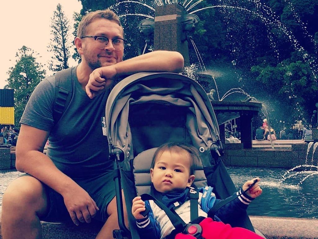 Mann sitzt mit einem Baby vor einem Brunnen.