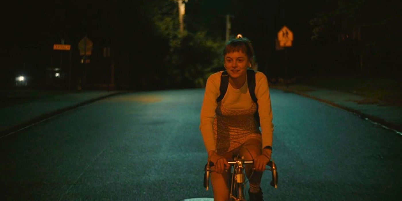 Emma Corrin als Darby radelt in „Ein Mord am Ende der Welt“ eine ruhige Straße entlang