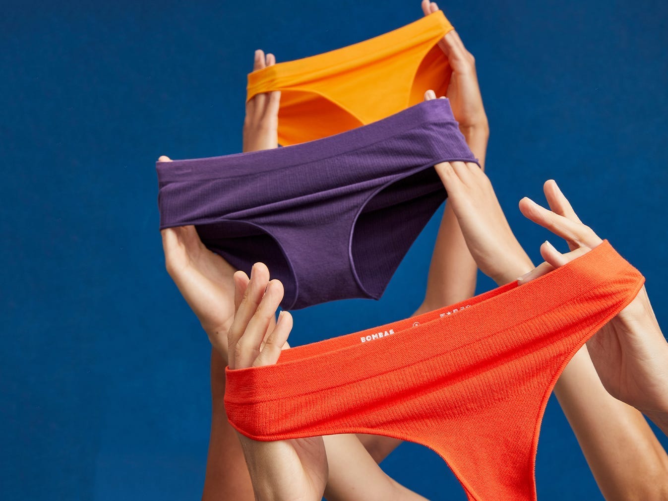 Hände halten Bombas-Unterwäsche in drei verschiedenen Stilen und Farben hoch.