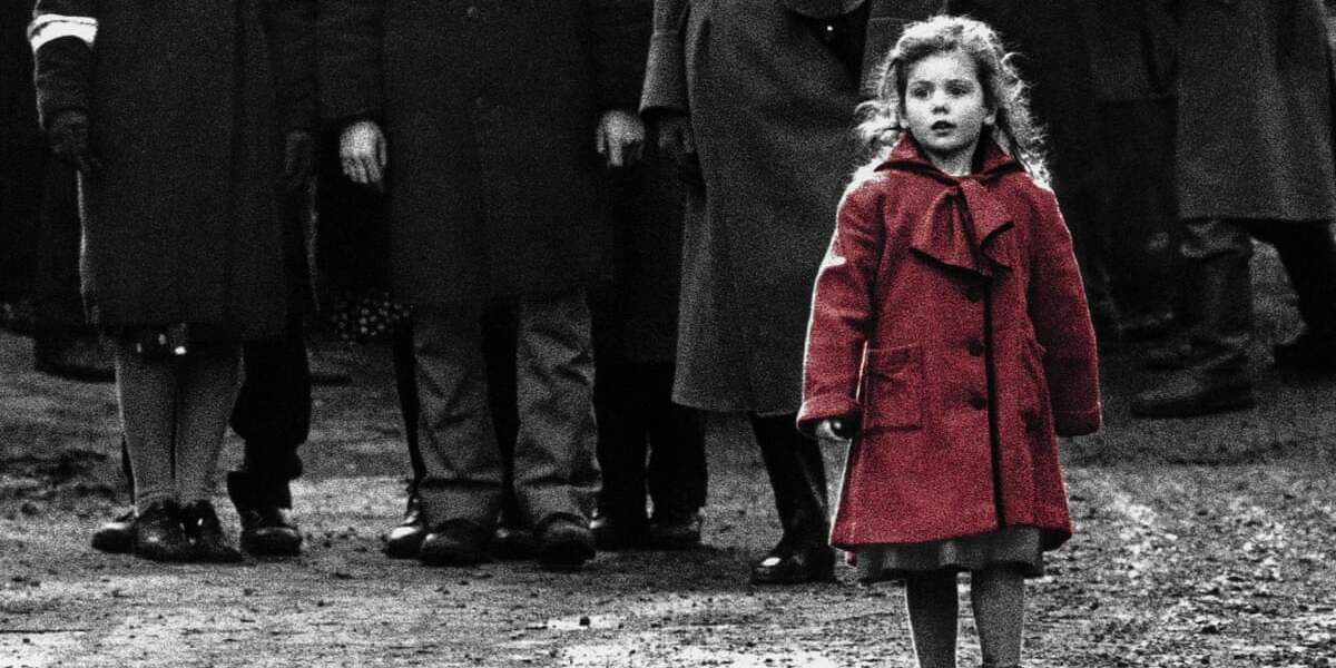 Das Mädchen im roten Mantel geht in Schindlers Liste mit Menschen hinter ihr durch die Straße