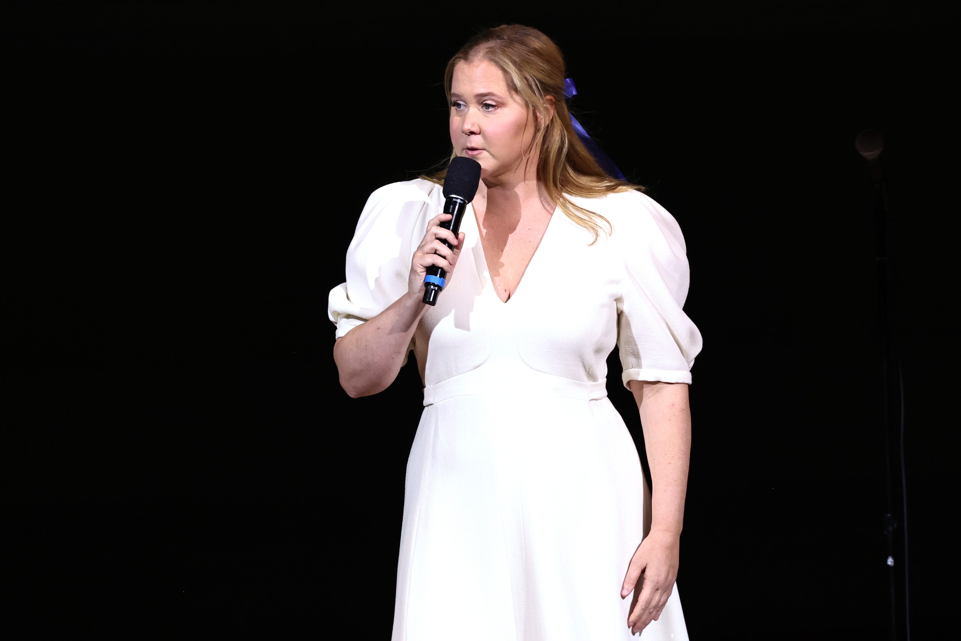 Amy Schumer tritt in einem weißen Kleid auf der Bühne auf.