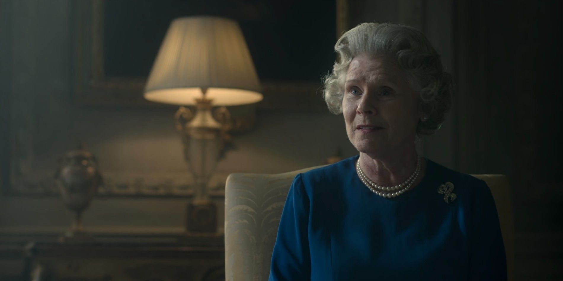 Imelda Staunton sitzt mit besorgtem Gesicht als Königin Elizabeth II. in Staffel 6 von The Crown auf einem Stuhl