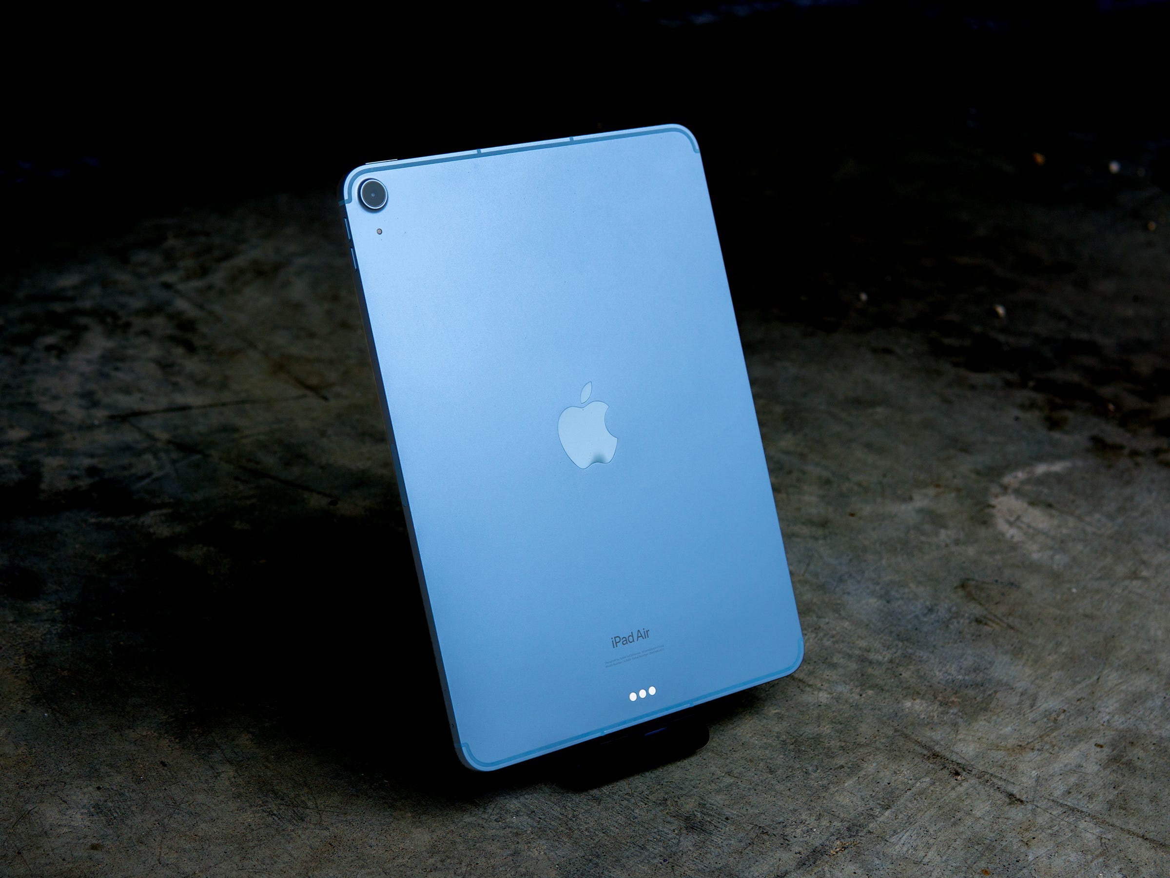 Das iPad Air 2022 steht auf einem Ständer und zeigt seine blaue metallische Rückseite in vertikaler Position.