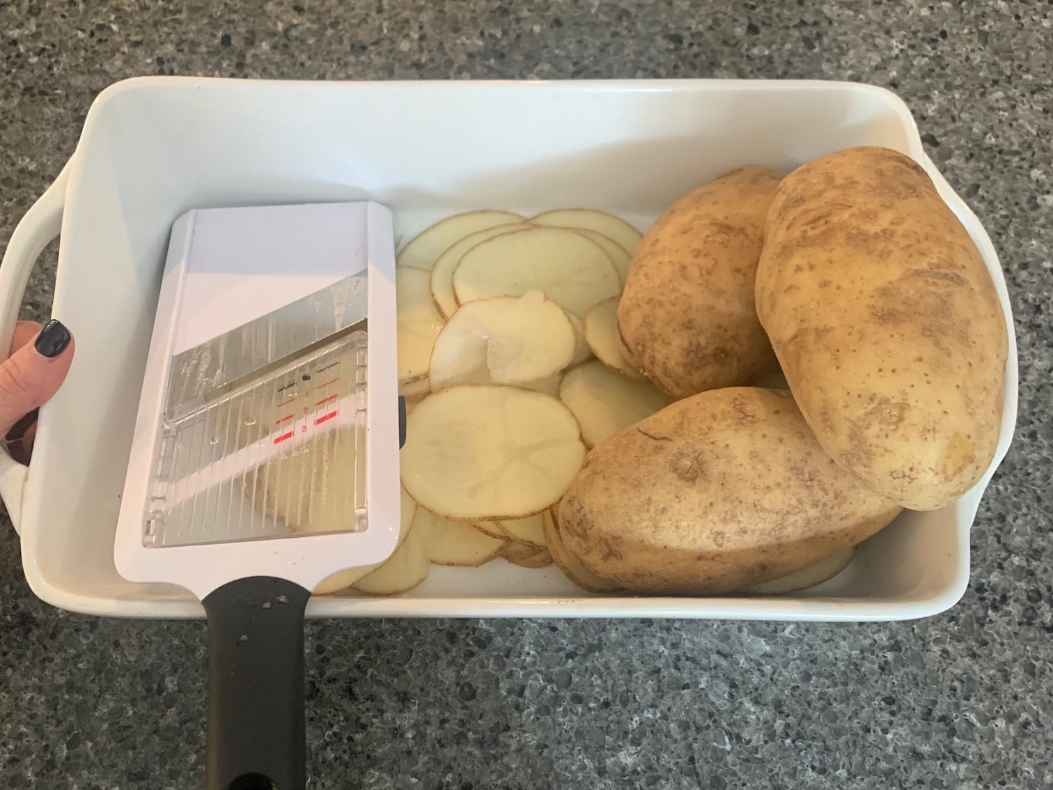 Kartoffeln und dünne Kartoffelscheiben in einem Behälter mit einer Mandoline