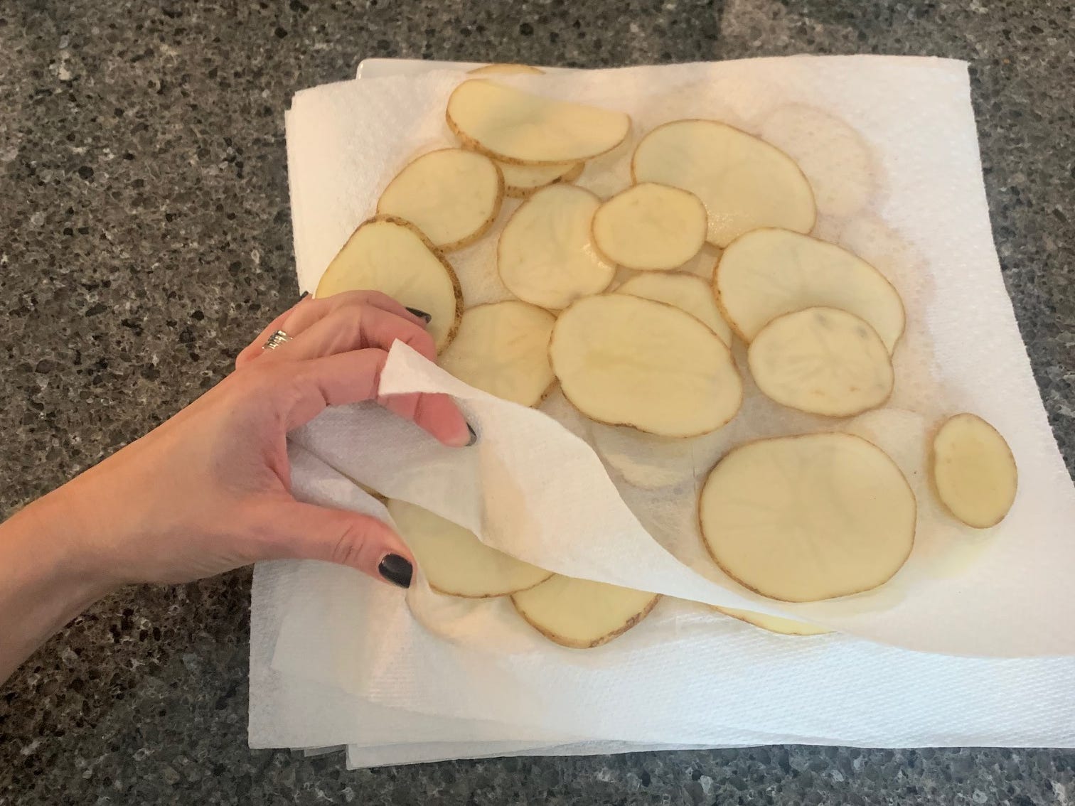 Kartoffelscheiben zwischen Lagen Papierhandtüchern auf einer Küchentheke