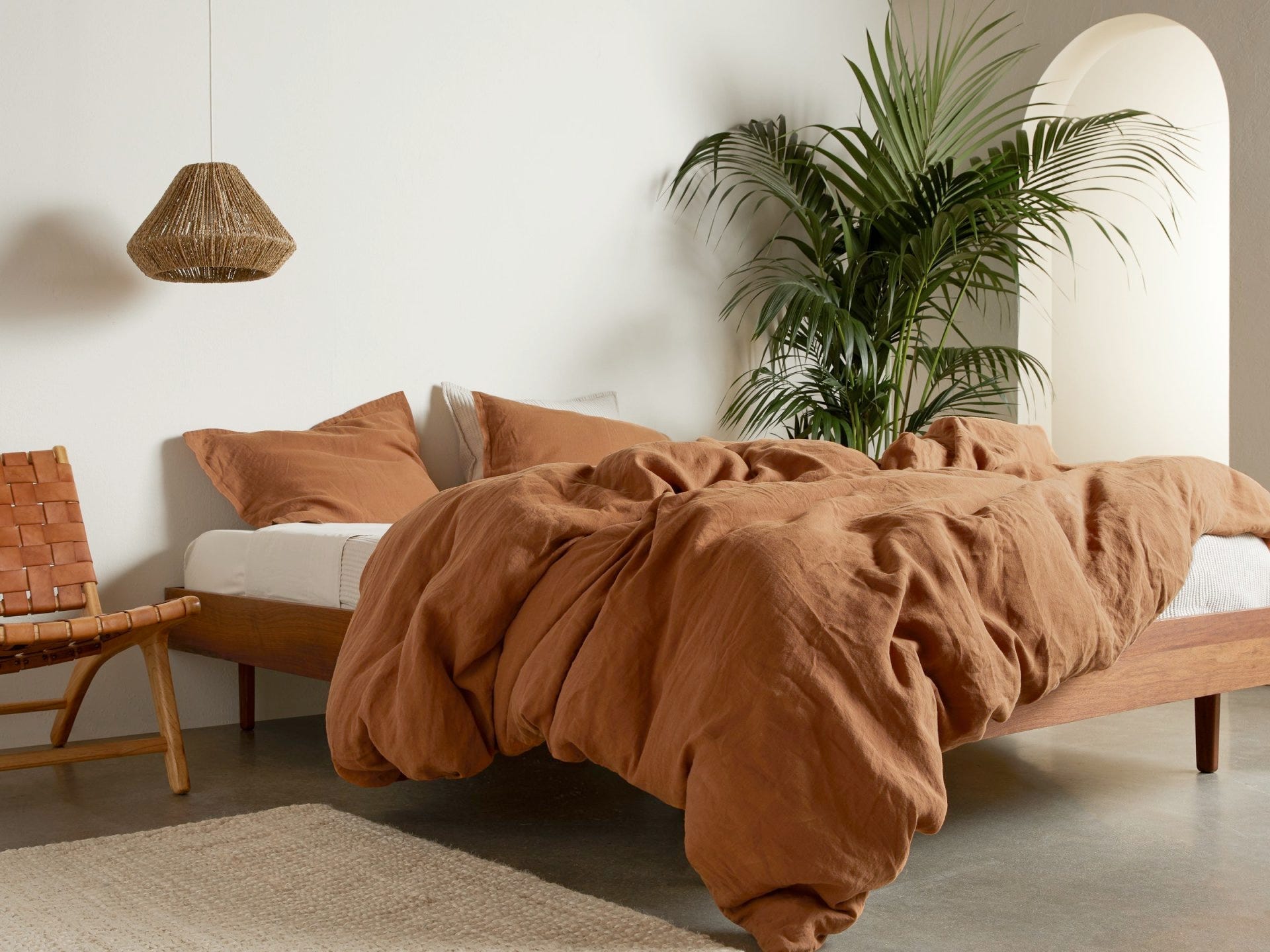 Ein Bett in einem Haus mit rostfarbener Bettdecke und Kissenbezügen von Parachute Home.