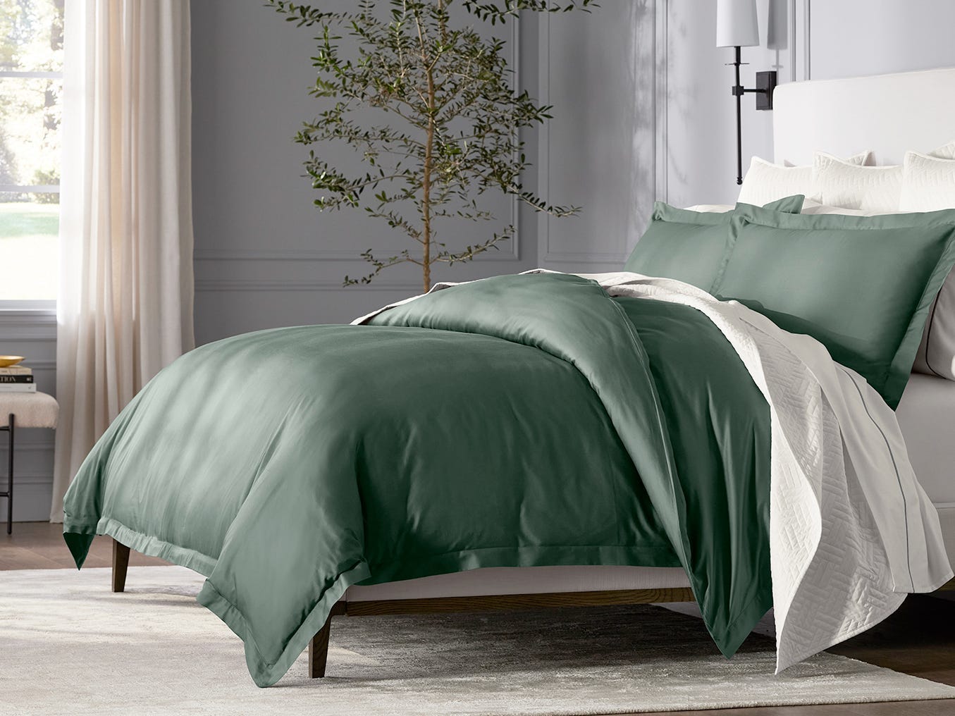 In einem Schlafzimmer ist ein Bett mit einer grünen Bettdecke und Kissen von Boll & Branch von der Seite zu sehen.