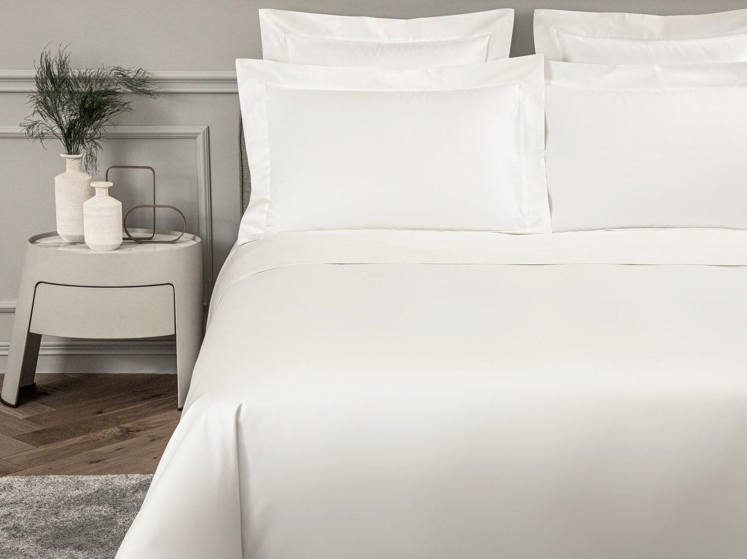 Ein Bett in einem Schlafzimmer ist mit einer weißen Bettdecke und Bettwäsche von Frette ausgestattet.