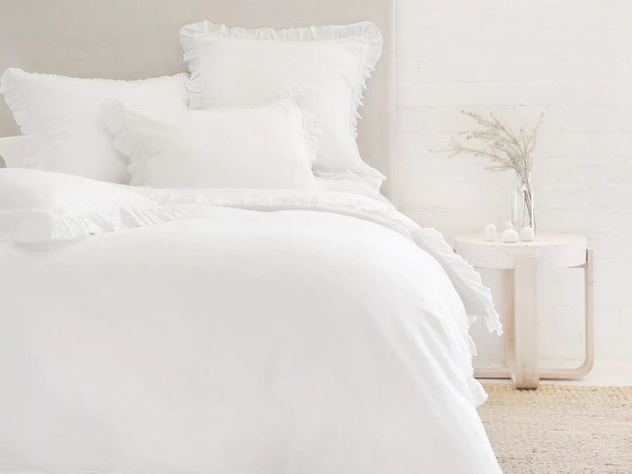 Ein Bett besteht aus weißen Laken und einer weißen Bettdecke mit Fransen von Pom Pom at Home.