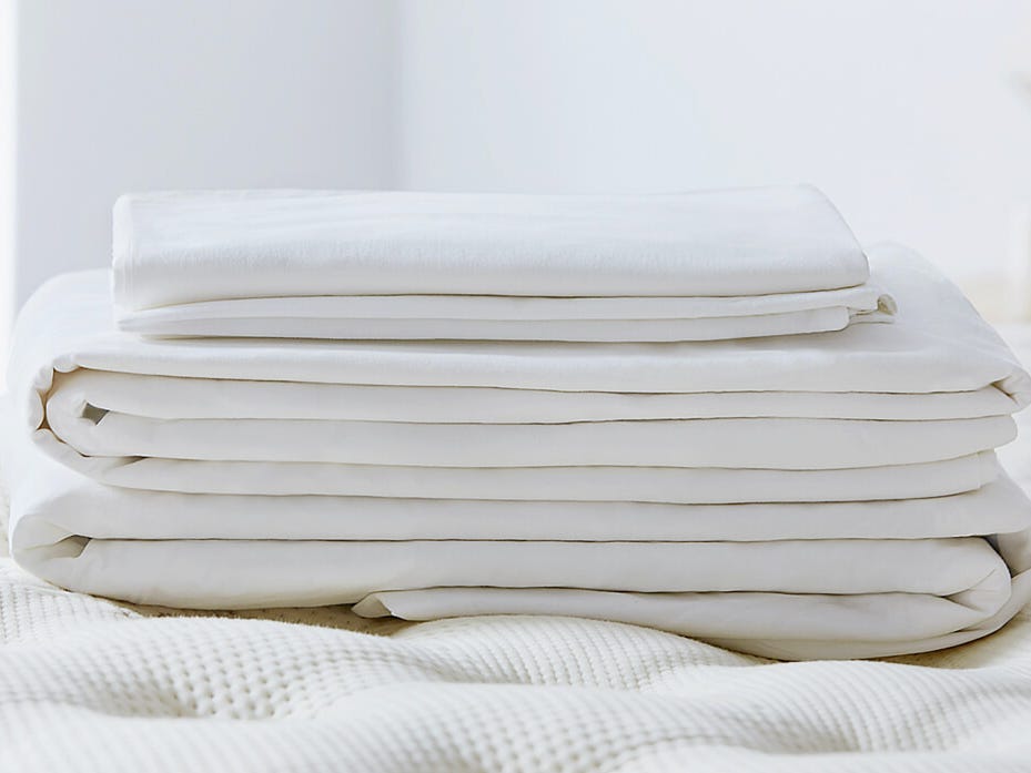 Ein Satz gefalteter weißer Laken von Saatva liegt auf einem Bett.