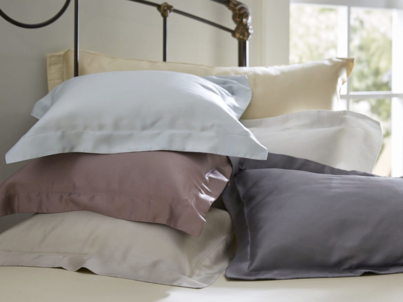 Auf einem Bett liegen mehrere Kissen in verschiedenfarbigen Kissenbezügen von SDH.