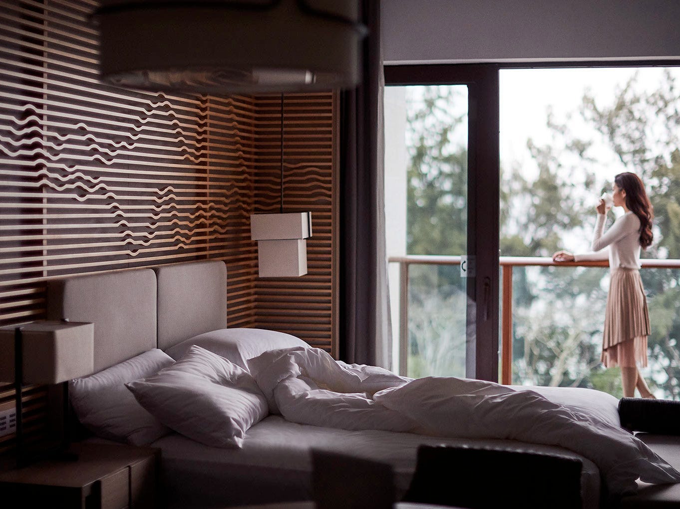 Innenraum eines Marriott-Hotelzimmers mit einem Bett aus weißen Laken und sichtbarer Person draußen auf dem Balkon.