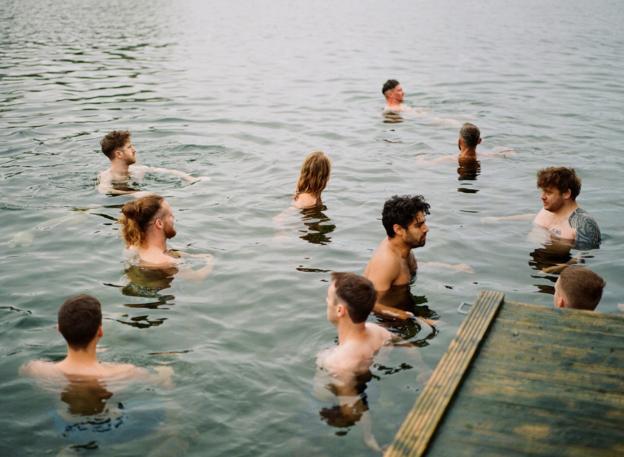 Eine Gruppe Männer schwimmt im offenen Wasser von einem Steg aus