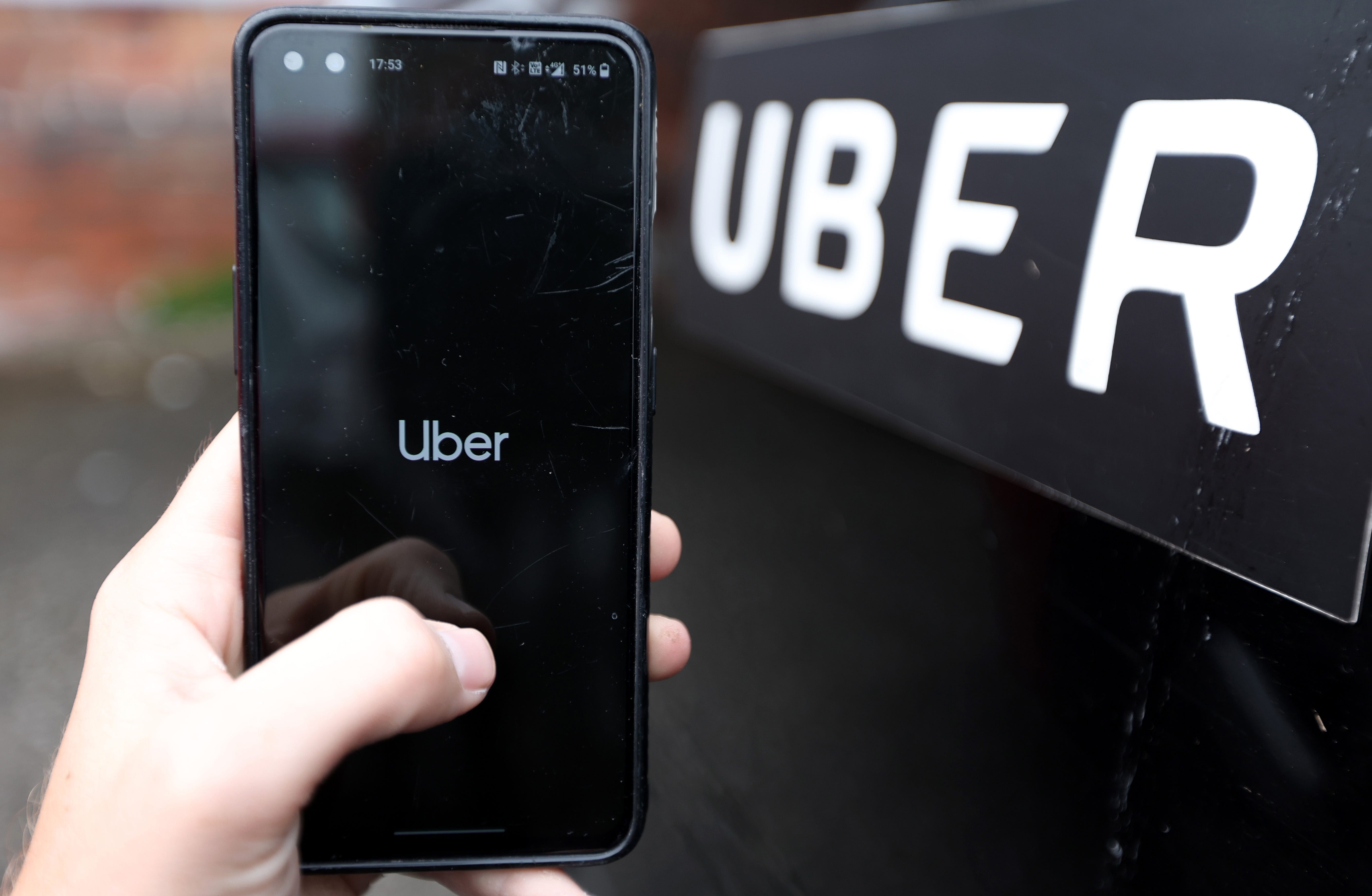 Eine Hand hält ein Telefon mit dem Uber-Logo auf dem Bildschirm vor einem Uber-Schild.