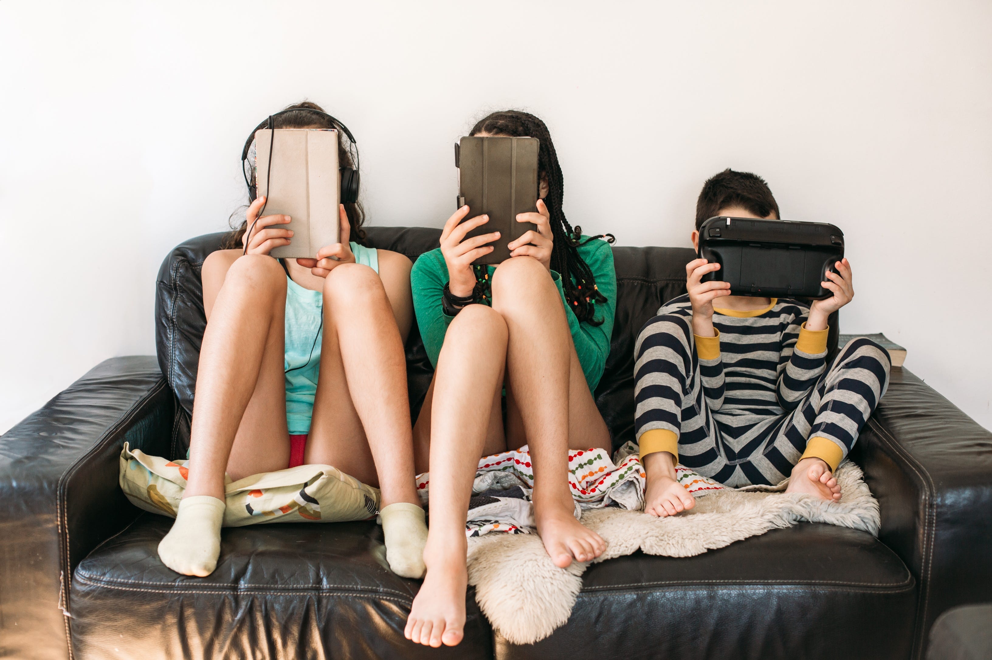 Drei Kinder mit elektronischen Geräten auf einem Sofa