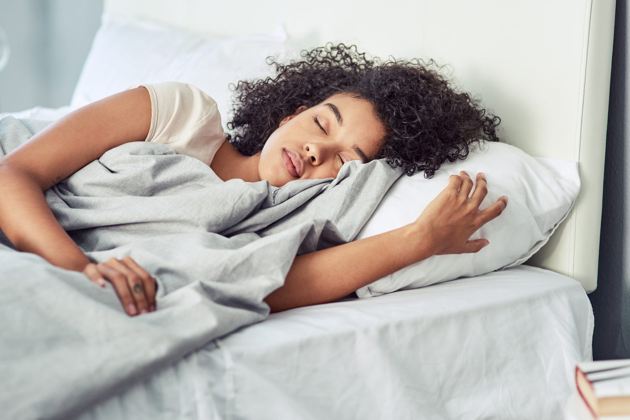 Eine junge Frau mit lockigem Haar schläft friedlich im Bett in einem sonnendurchfluteten Raum