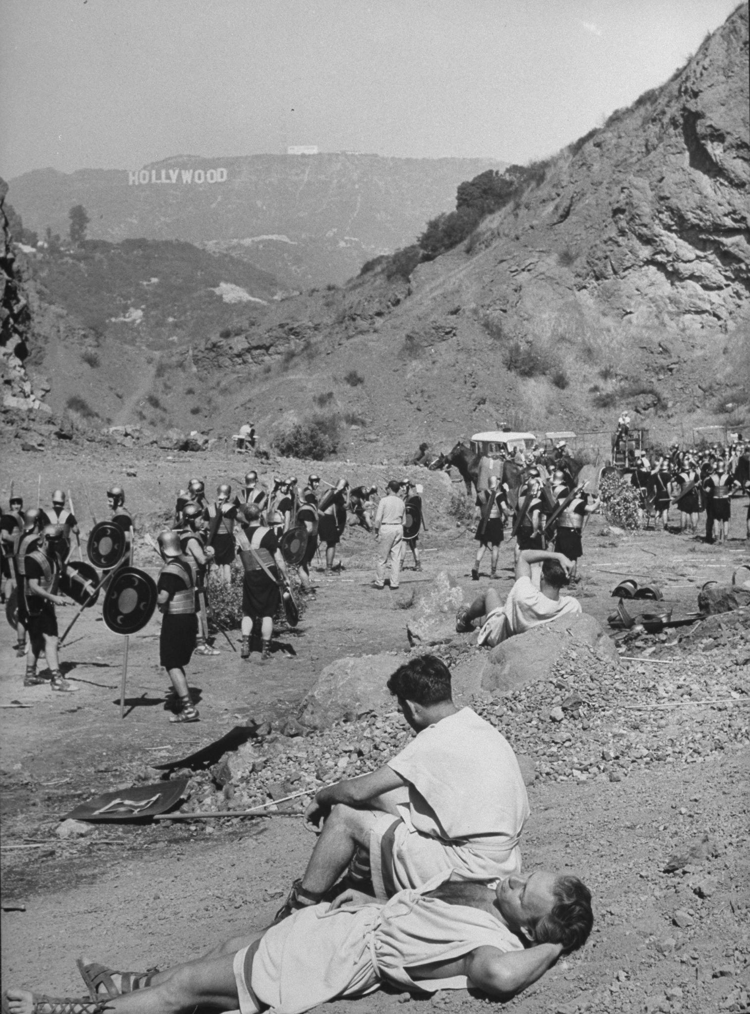 Extras zeigen römische Soldaten, die in einem baumlosen Tal ruhen, mit dem Hollywood-Schild auf einem Hügel im Hintergrund während der Dreharbeiten zu Julius Cäsar.