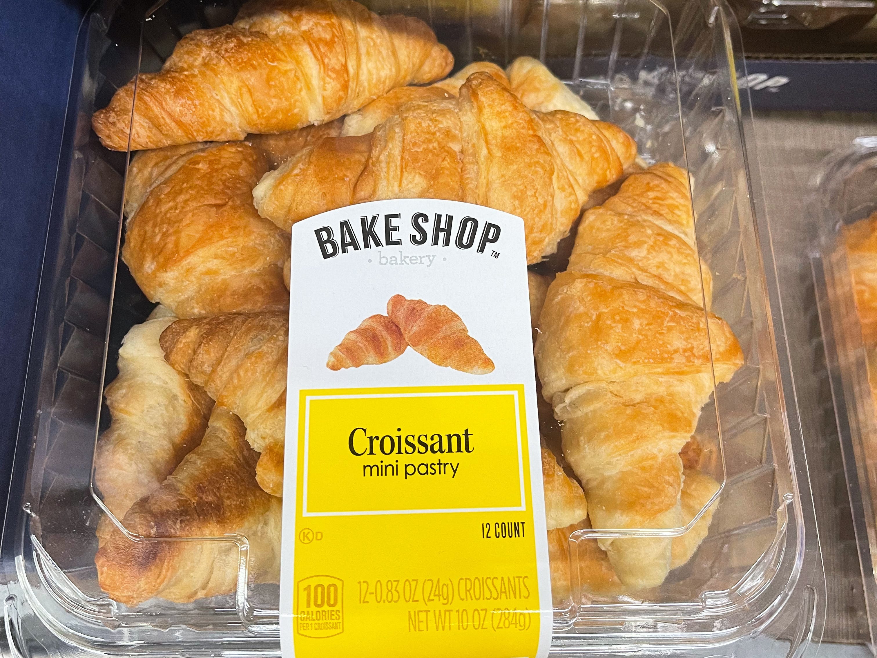 Ein Plastikbehälter mit Croissants mit einem weiß-gelben Etikett mit der Aufschrift „Bake Shop“.