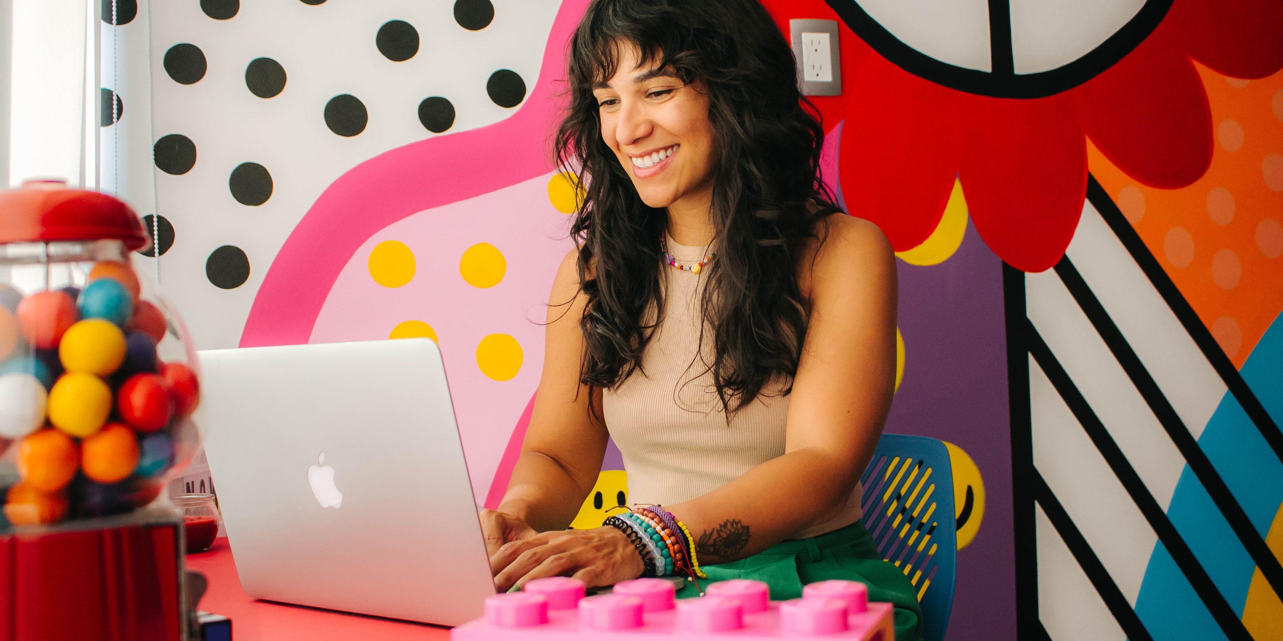 Andrea Valeria sitzt mit einem Macbook an ihrem Schreibtisch vor einem bunten Wandgemälde