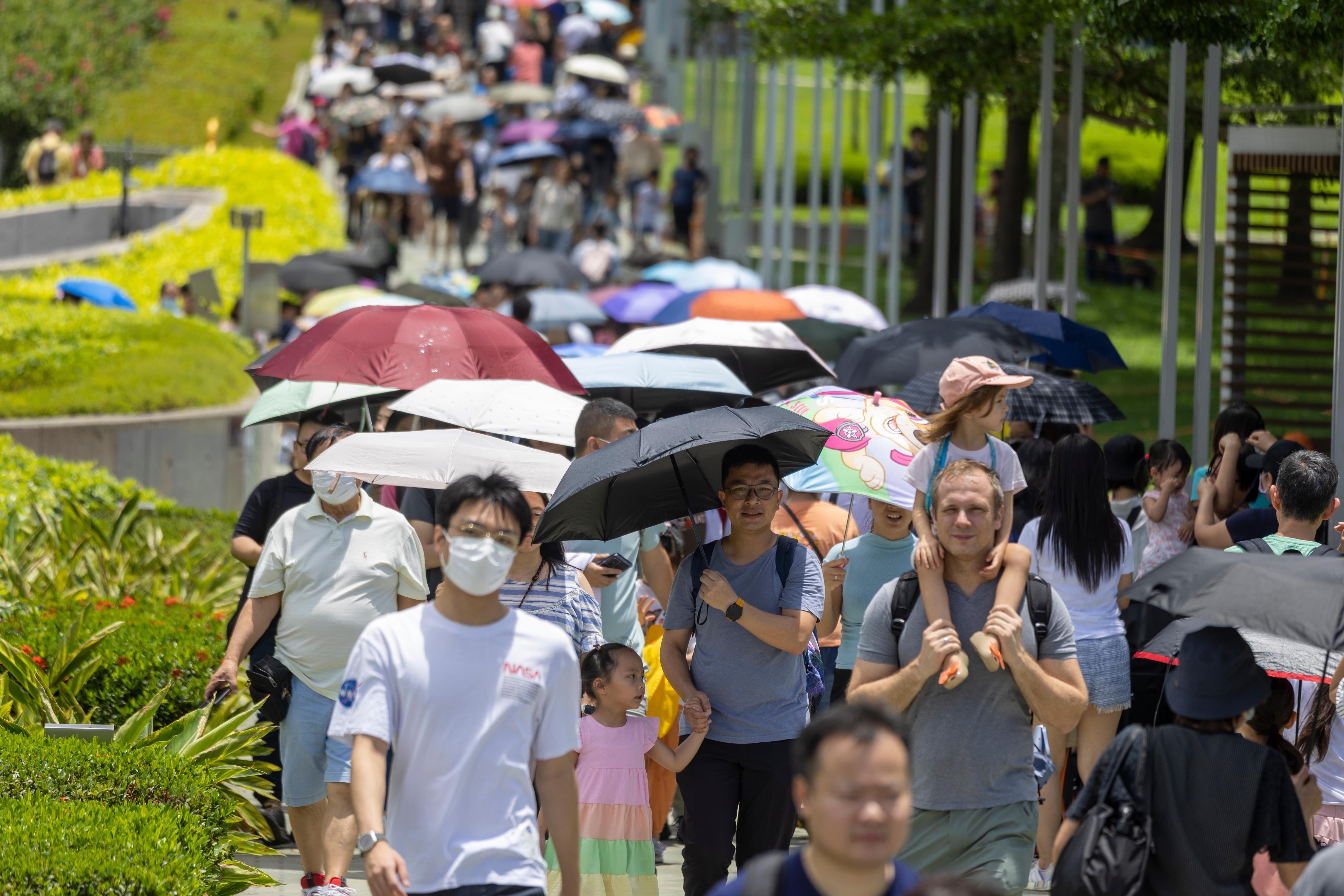 Menschen, die an einem sonnigen Tag mit Regenschirmen in Hongkong spazieren gehen.