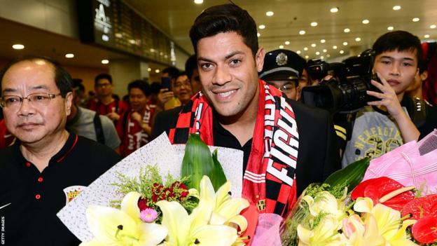 Hulk lächelt, als er mit einem Blumenstrauß und einem Shanghai SIPG-Schal durch einen überfüllten Flughafen geht