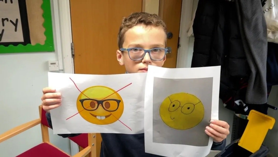 Teddy hält das aktuelle beleidigende Nerd-Gesichts-Emoji mit seinem eigenen Ersatz-Genie-Emoji auf der rechten Seite hoch.  Bildnachweis BBC – Der 10-jährige Teddy startet eine Petition, um Apple dazu zu bringen, anstößige Emojis zu ändern