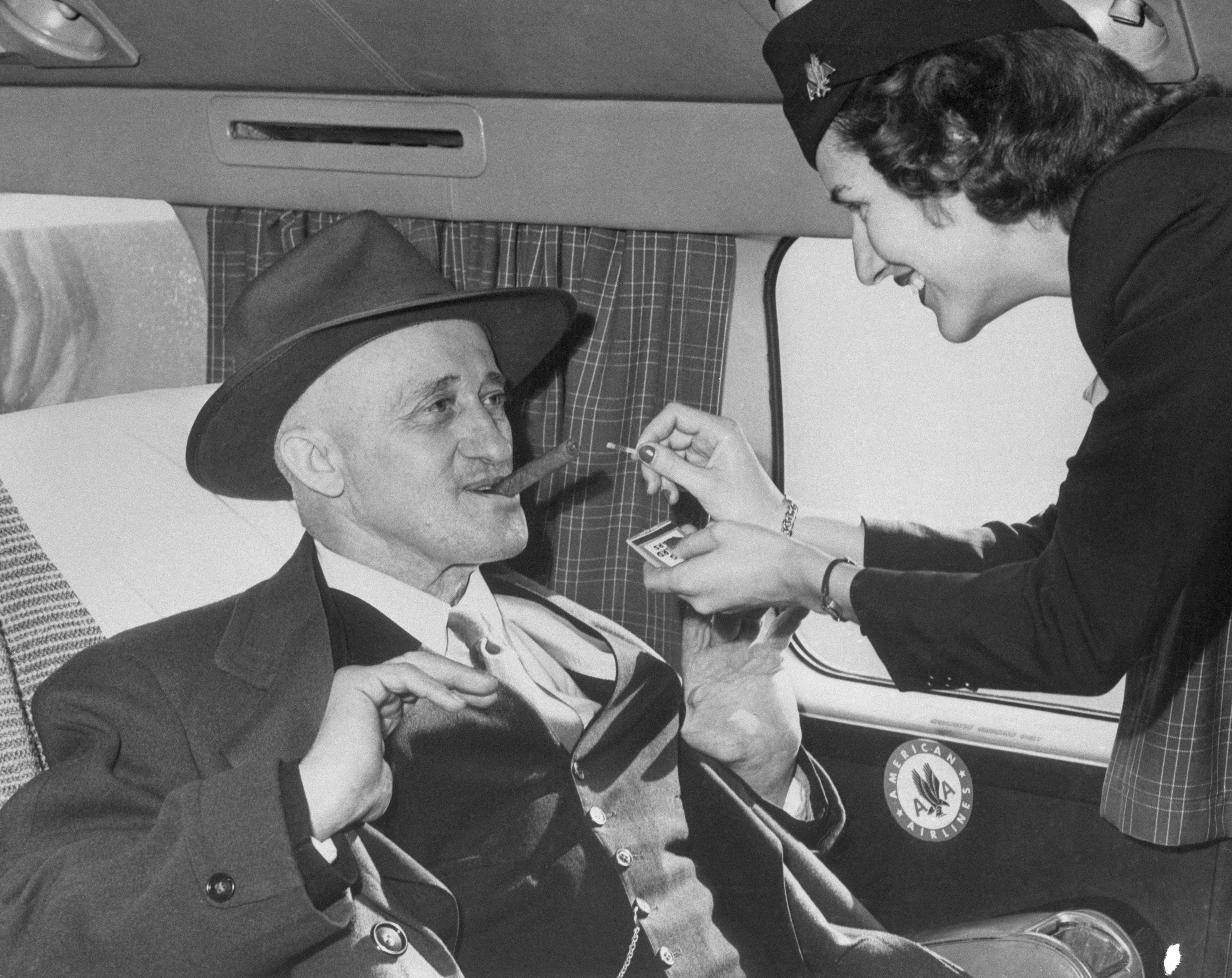 Ein Flugbegleiter zündet 1949 in einem Flugzeug einem Mann die Zigarre an
