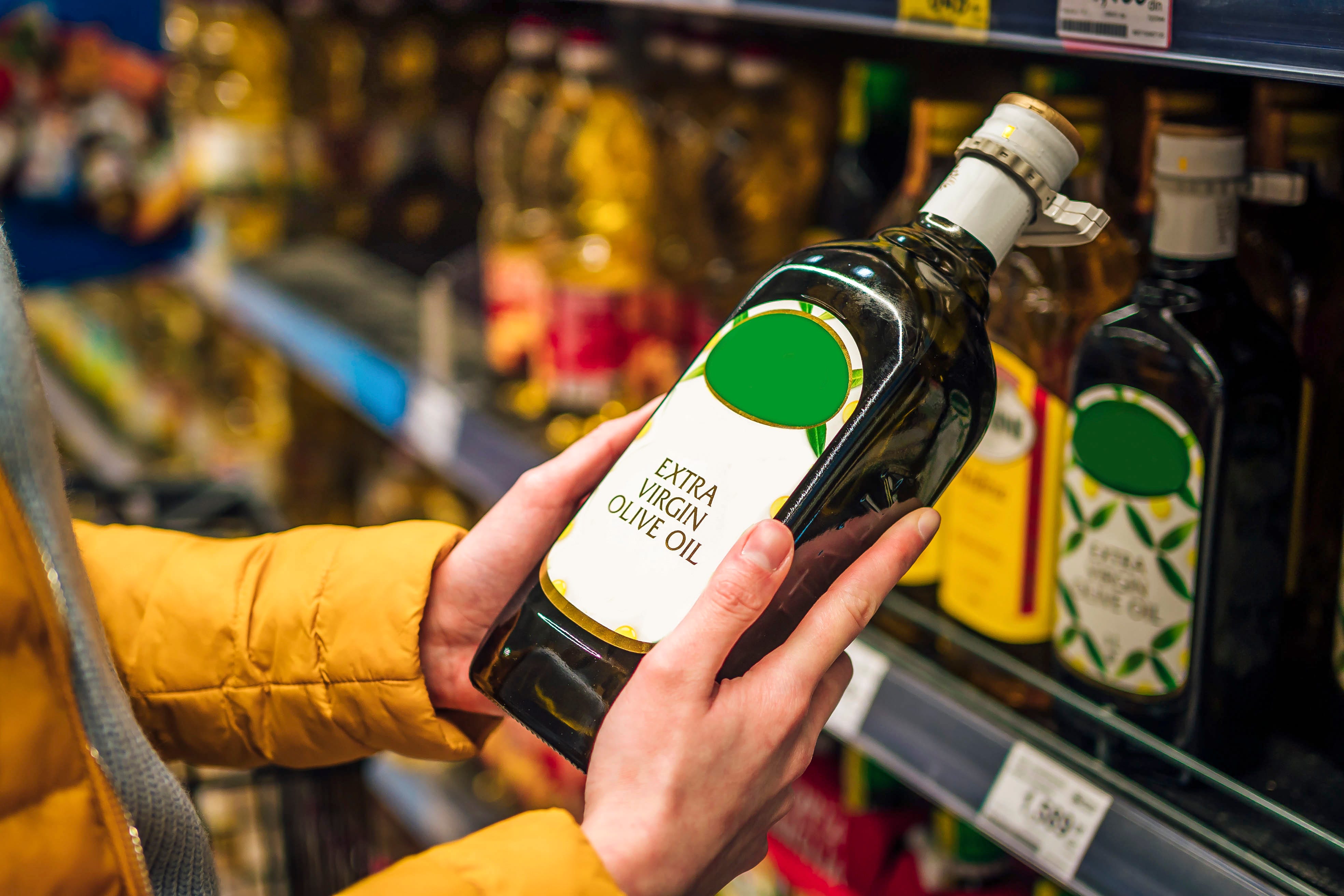 Eine Frau wählt eine Flasche natives Olivenöl extra aus einem Supermarktregal