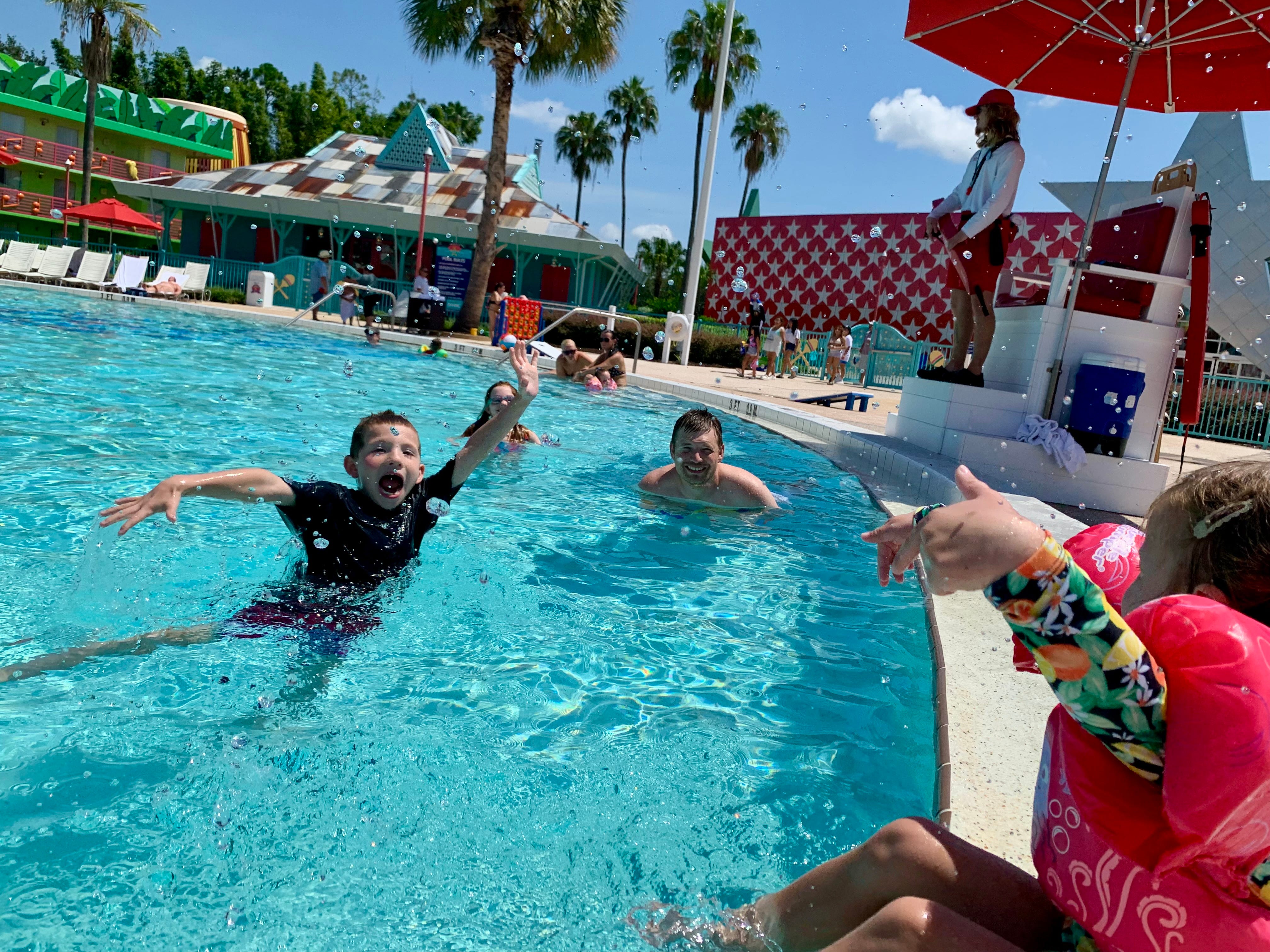 Kinder spielen im Pool des Disney All-Star Music Resorts mit Rettungsschwimmer an der Seite