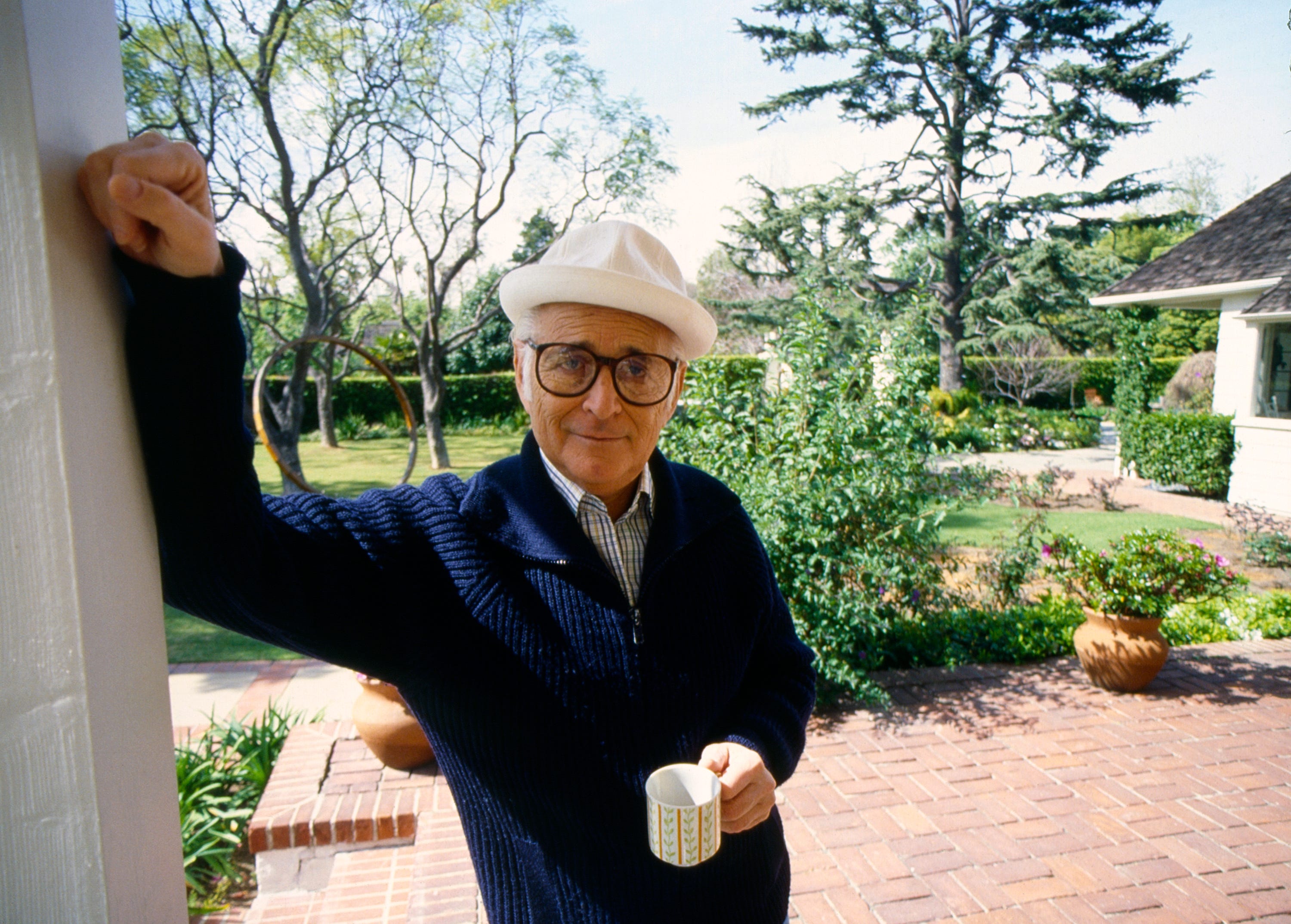 Norman Lear hält eine Kaffeetasse in der Hand und lehnt an der Seite einer Tür