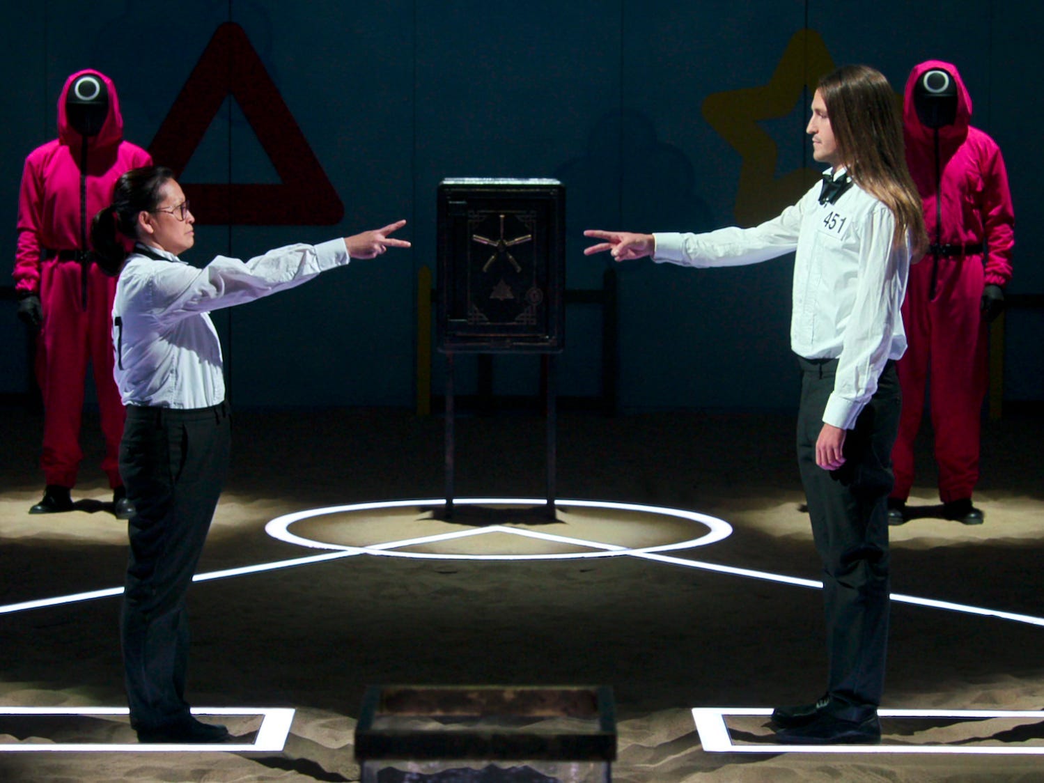 Mai Whelan und Phill Cain in formeller Kleidung zeigen sich in „Squid Game: The Challenge“ mit der Schere ein Handzeichen.