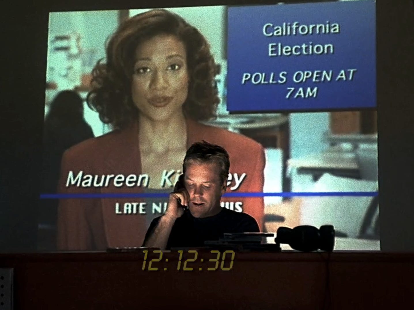 Kiefer Sutherland als Jack Bauer in „24“, er steht vor einer an die Wand projizierten Nachrichtensendung und telefoniert