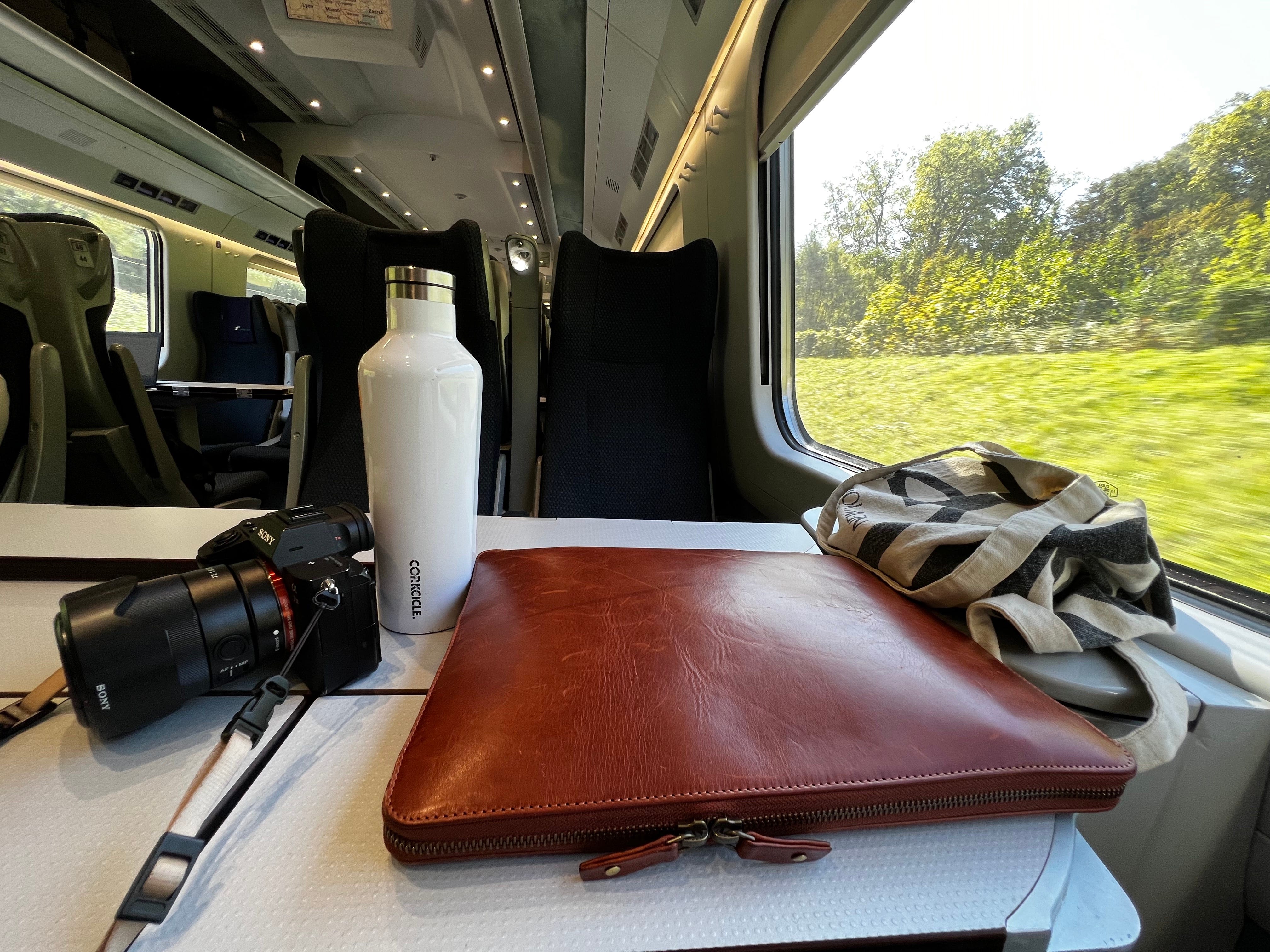 Kelseys Kamera, Wasserflasche und Laptoptasche auf einem Tisch vor ihrem Zugsitz