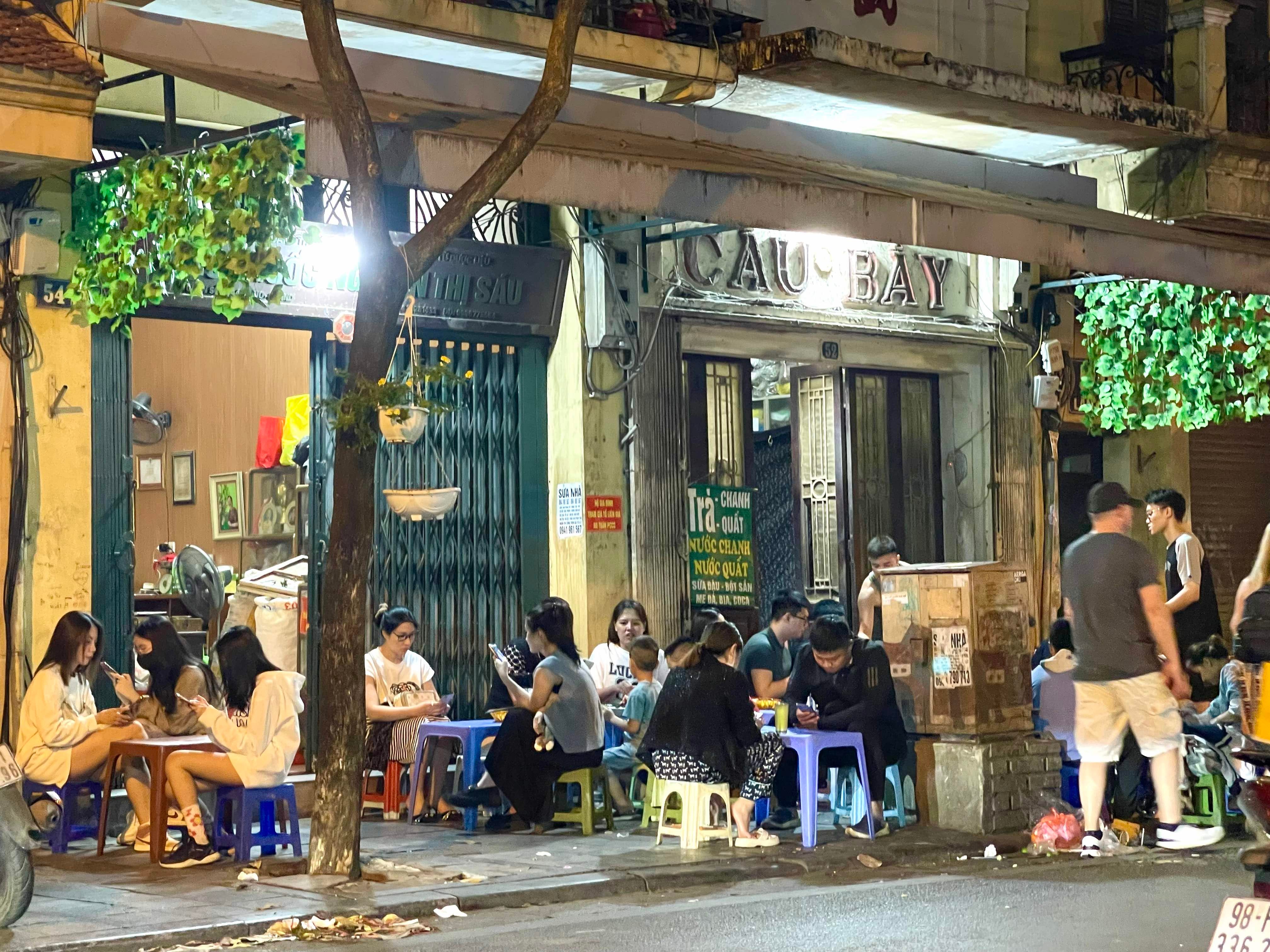 Menschen sitzen auf Hockern in Hanoi und essen Straßenessen.