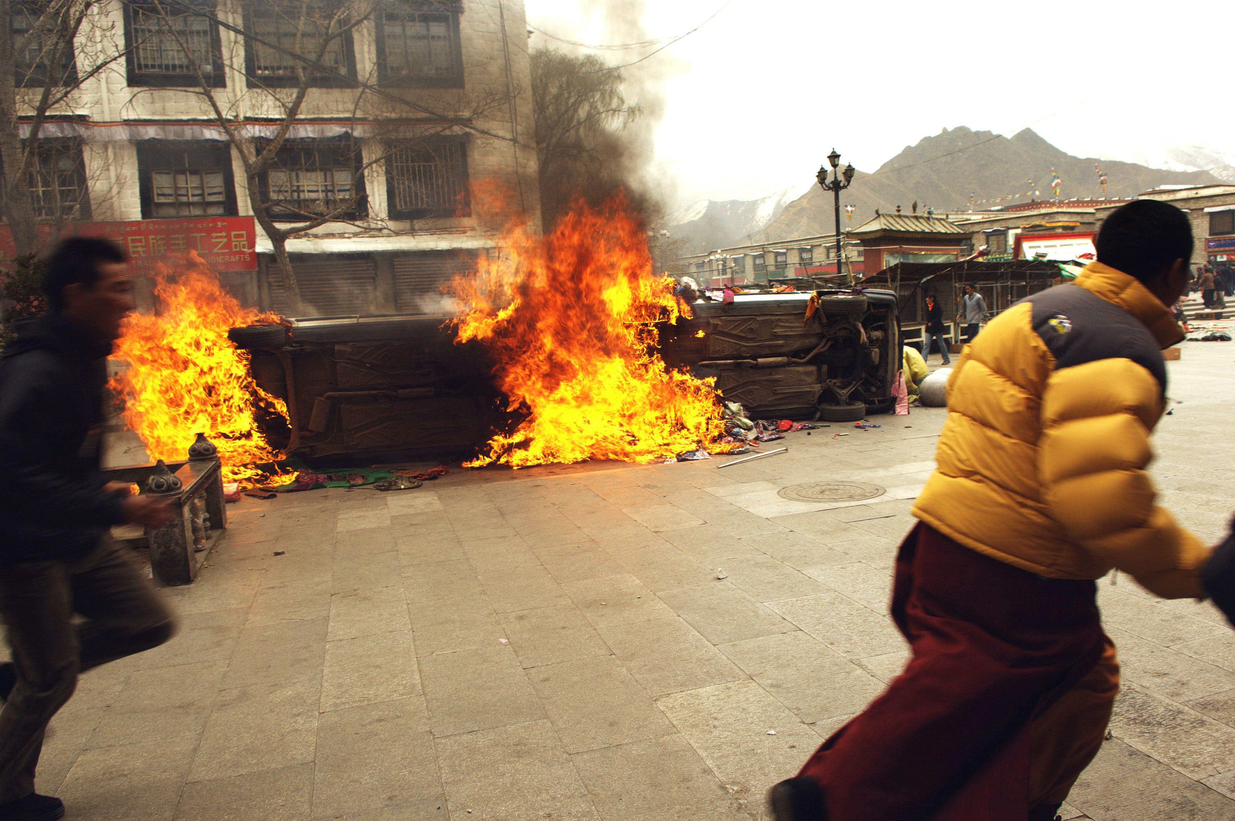 Das am 22. März 2008 aufgenommene Foto zeigt einen Tibeter, der am 14. März 2008 in Lhasa an brennenden Fahrzeugen vorbeiläuft, als in der tibetischen Hauptstadt tödliche Gewalt ausbrach und Sicherheitskräfte mit Schüssen die größten Proteste gegen die chinesische Herrschaft seit zwei Jahrzehnten niederschlugen.