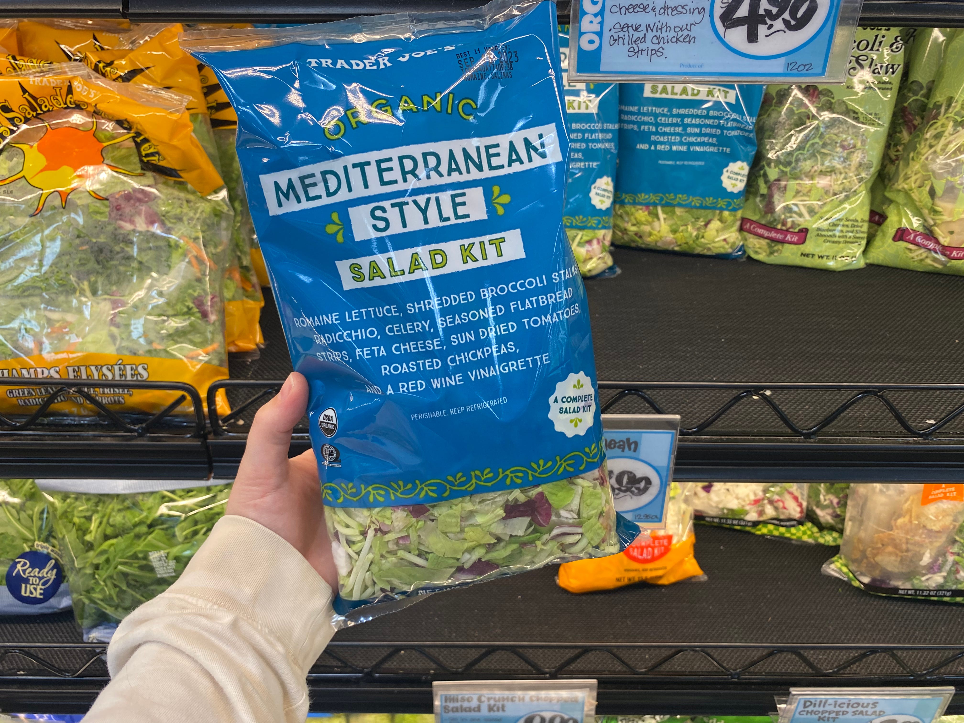 Hand hält eine Tüte Bio-Salatset im mediterranen Stil in den Gängen bei Trader Joes hoch