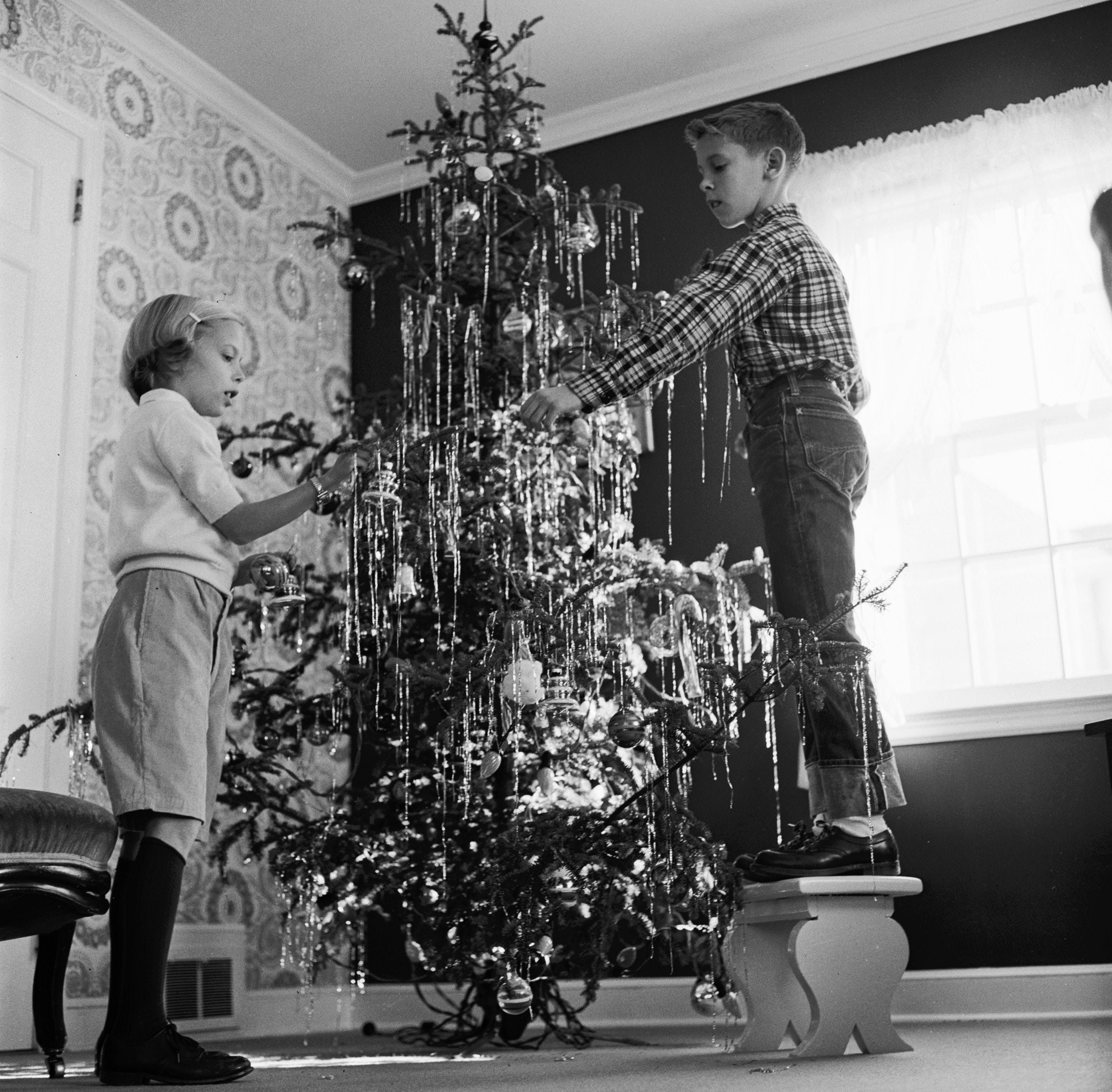 Ein Junge und seine Schwester schmücken 1955 einen Weihnachtsbaum mit Lametta