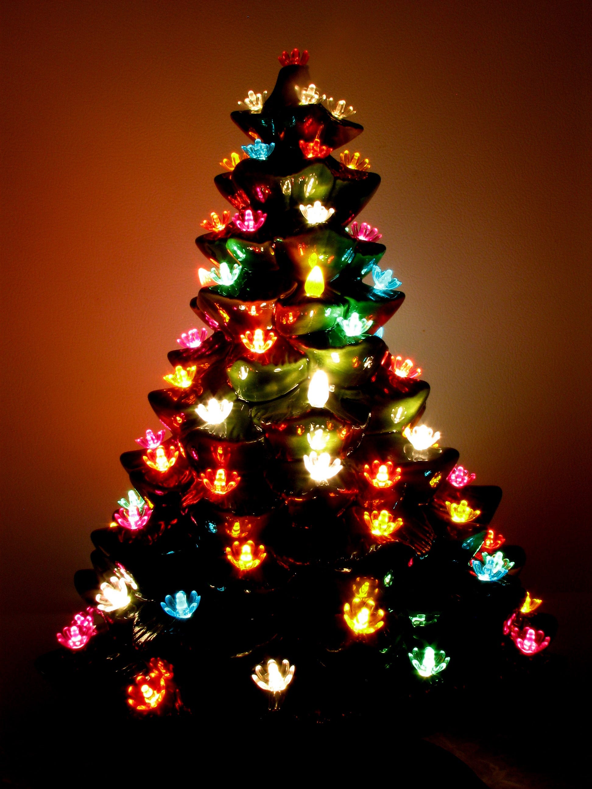Vintage-Weihnachtsbaum aus glasierter Biskuitkeramik auf dem Tisch mit mehrfarbigen Lichtern im Dunkeln.
