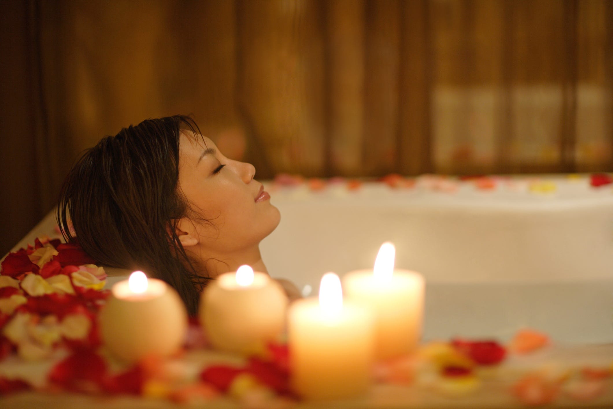 Frau nimmt ein Bad mit Kerzen und Blütenblättern